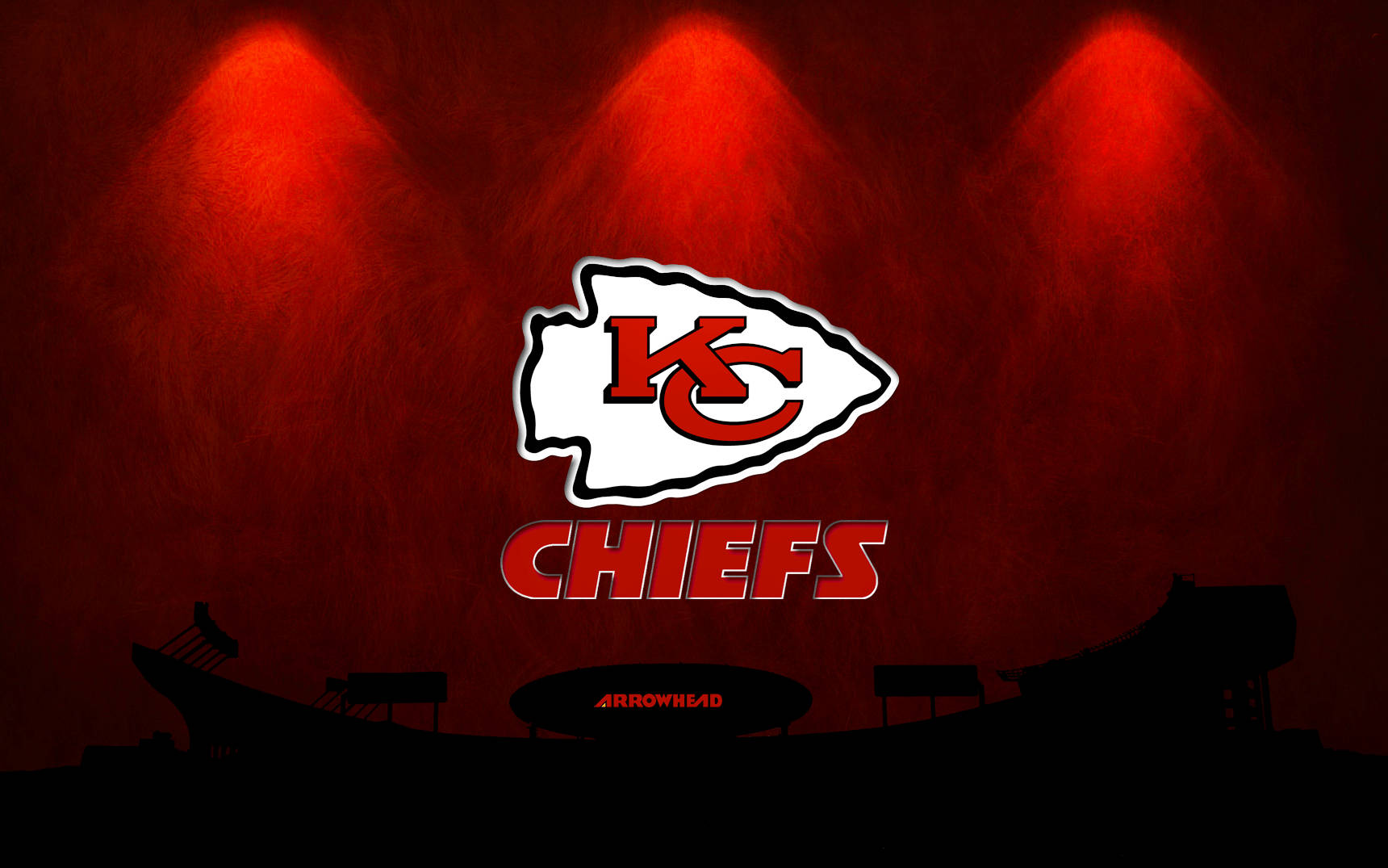 Kc Chiefs 桌布 壁紙 — 堪薩斯城酋長隊標誌在黑暗的體育場輪廓背景下被紅色聚光燈照亮。