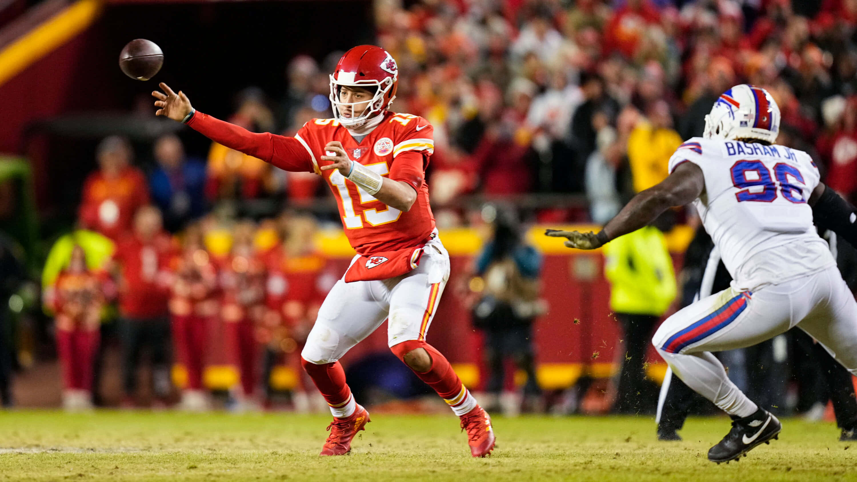 NFL 桌布 壁紙 — 堪薩斯城酋長隊的紅色四分衛擲出橄欖球，而水牛城比爾隊的白色防守球員在燈光球場上撲向他要擒抱。