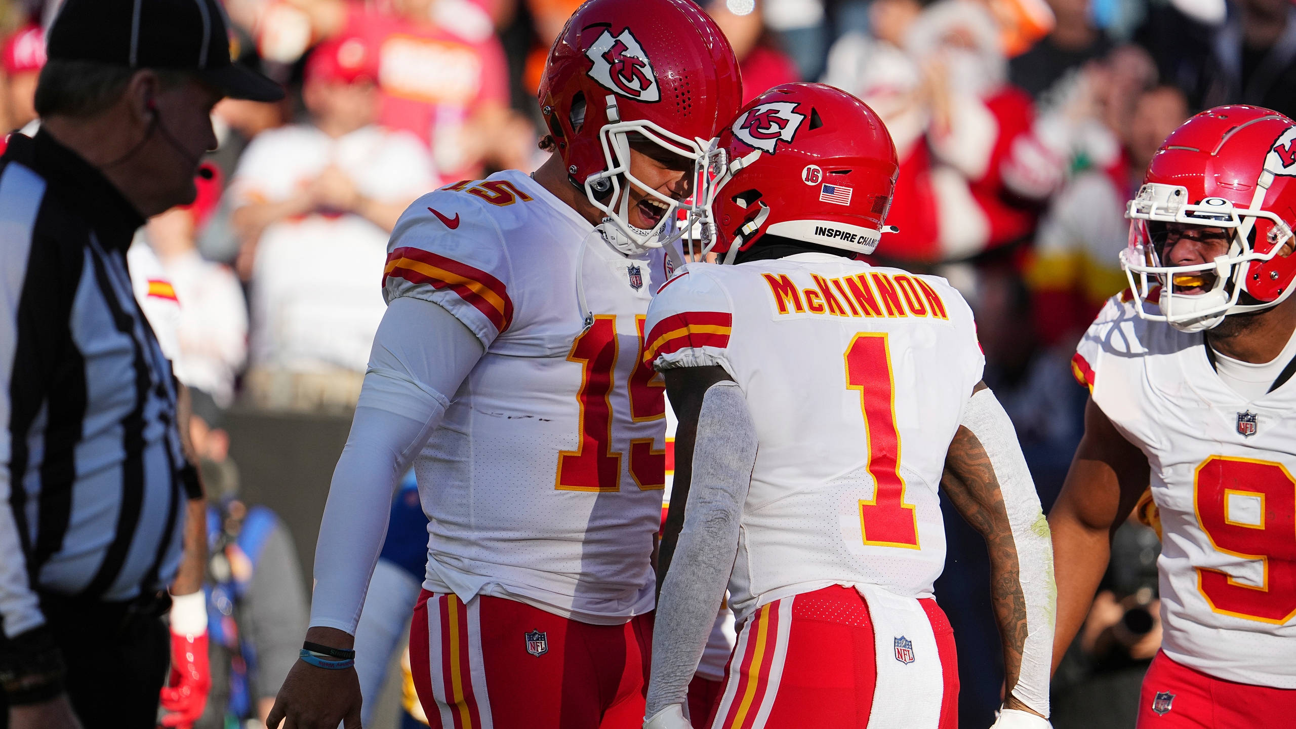 Kansas City Chiefs Cool 桌布 壁紙 — 堪薩斯城酋長隊的足球員身穿紅、白、黃色球衣，在陽光明媚的比賽日場地上圍成一圈，附近有裁判。