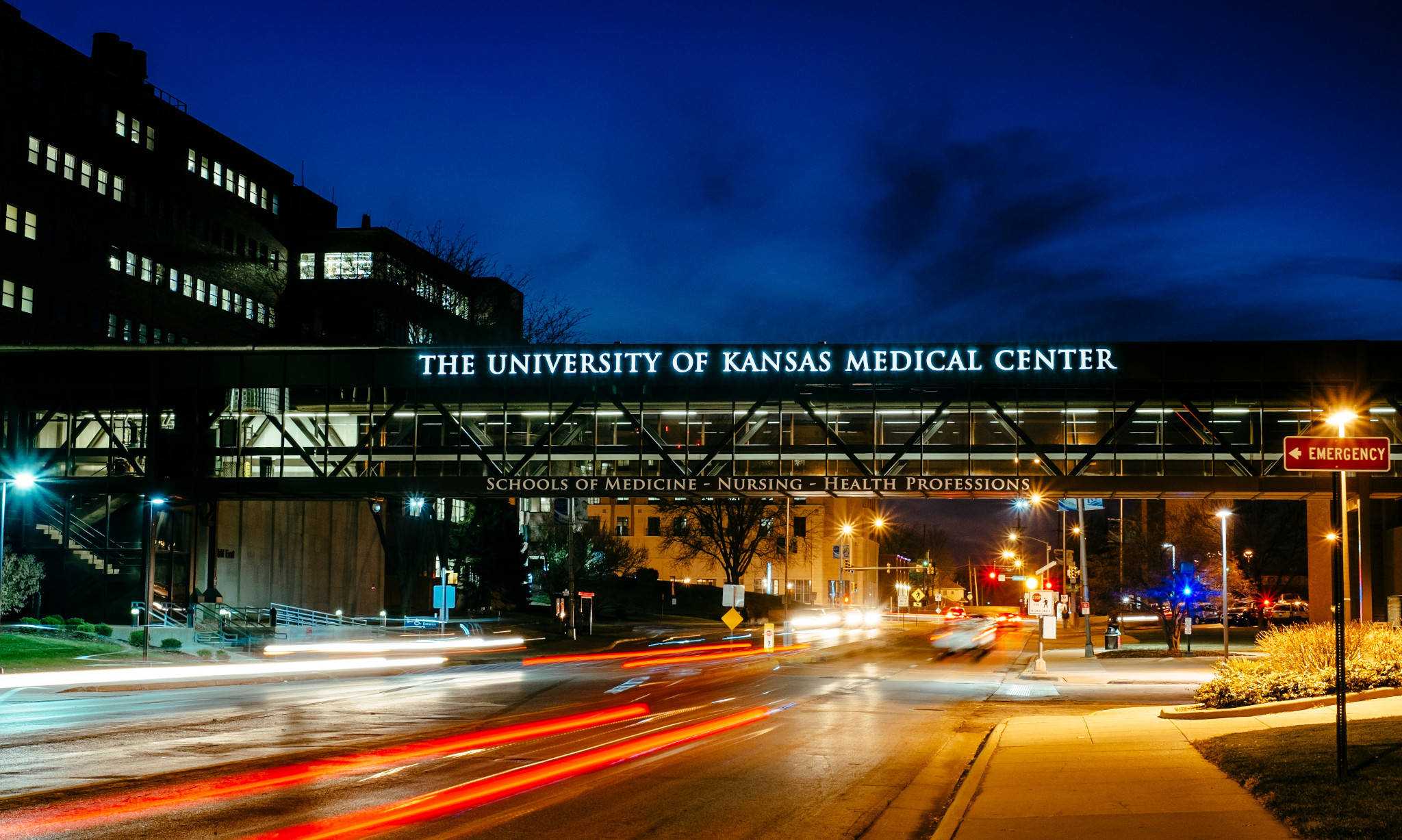 Hospital 桌布 壁紙 — 堪薩斯大學醫學中心的長時間曝光夜景，流動的車燈和發光的標誌在深藍色天空的襯托下格外醒目。
