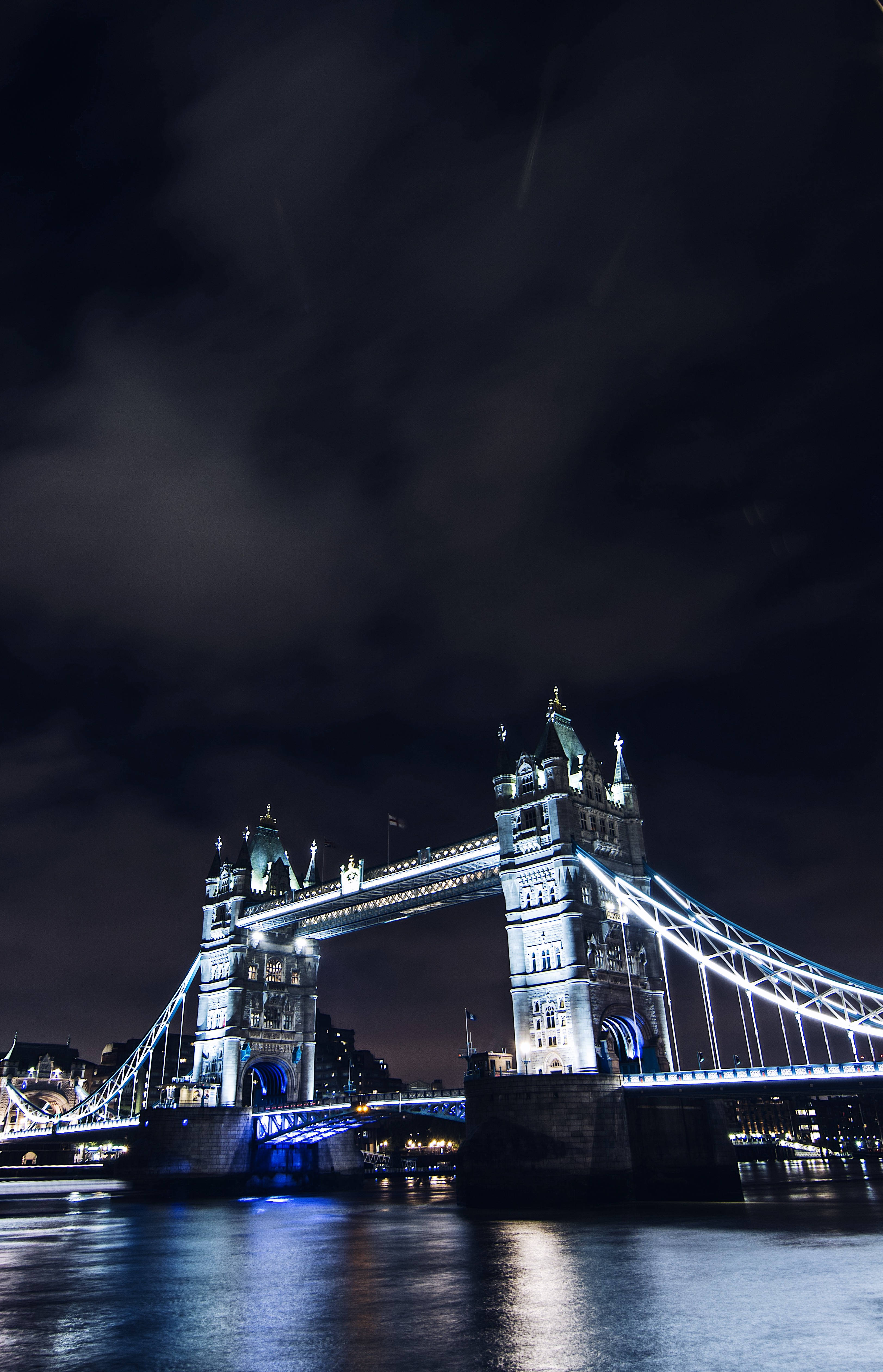 bridge 桌布 壁紙 — 塔橋在夜間被藍色燈光照亮，倒映在泰晤士河上，天空陰暗多雲。