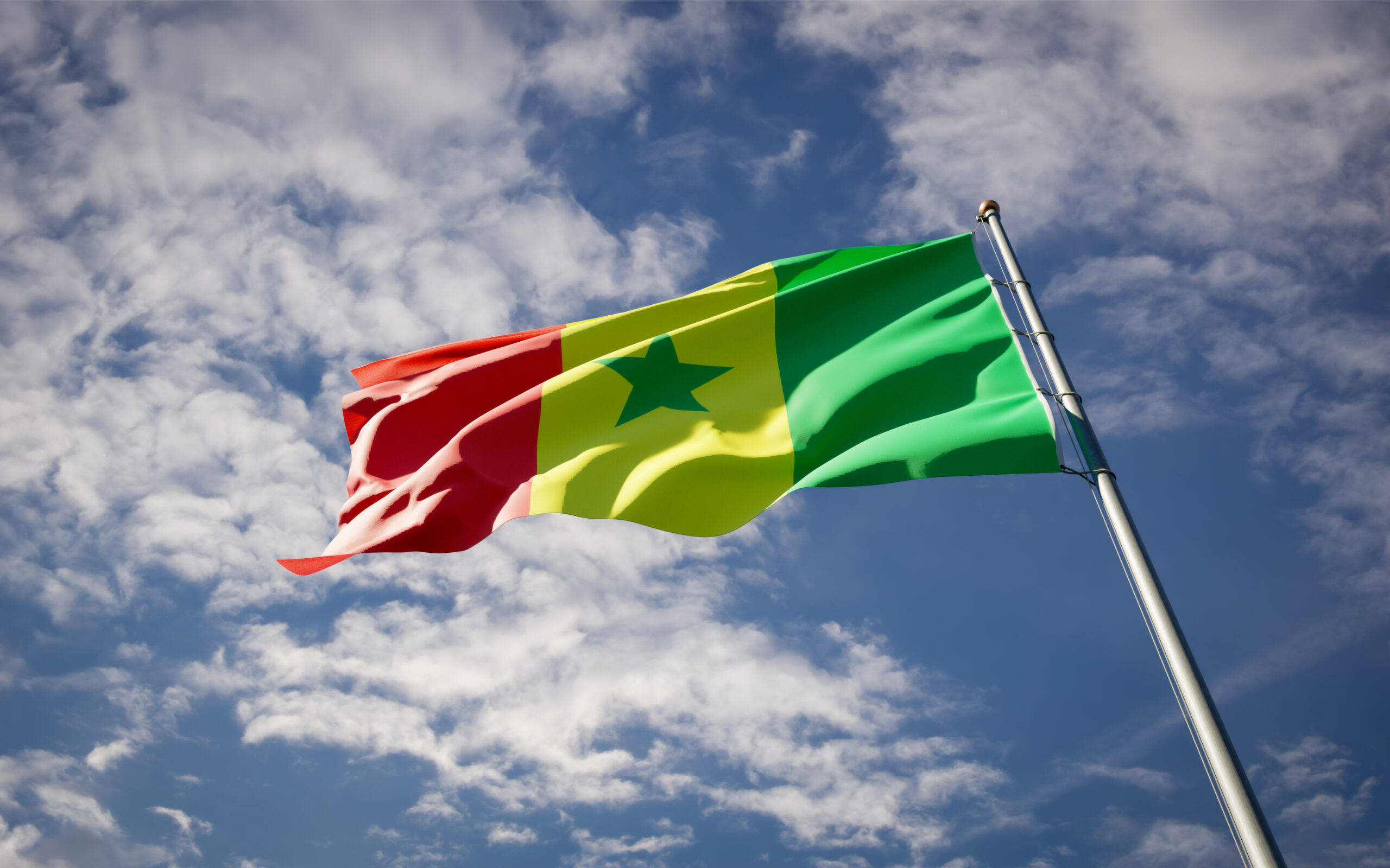 Senegal 桌布 壁紙 — 塞內加爾國旗，帶有紅、黃、綠條紋和一顆綠色星星，在佈滿蓬鬆白雲的明亮藍天下自豪地飄揚。
