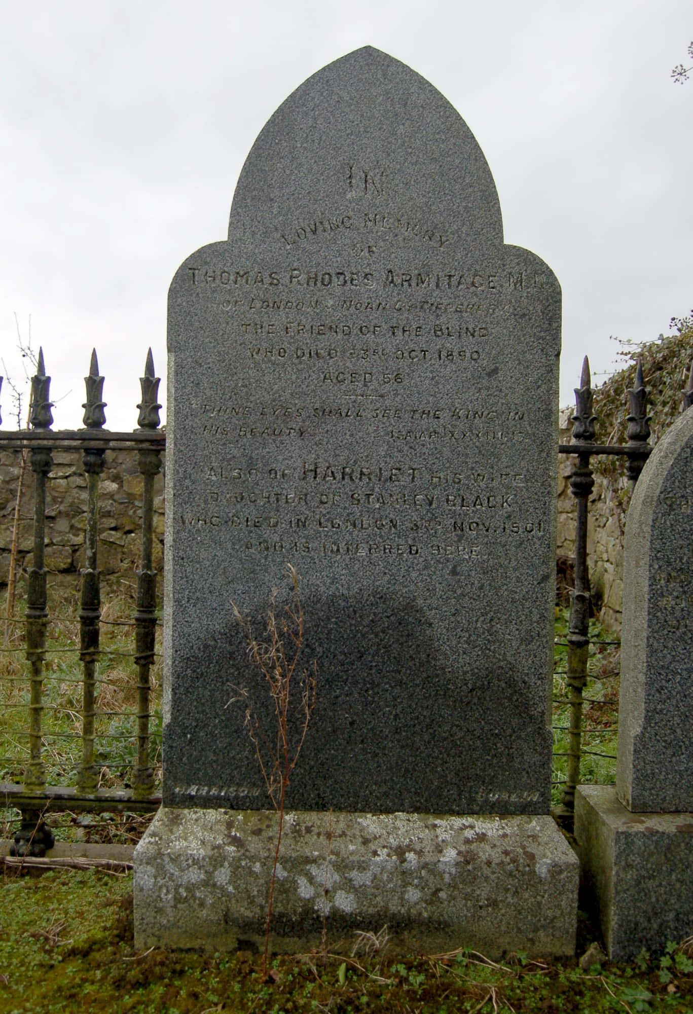 Gravestone 桌布 壁紙 — 墓園中一塊風化的灰色墓碑，刻有姓名和日期，周圍是長滿苔蘚的草地和鍛鐵圍欄，天空多雲。