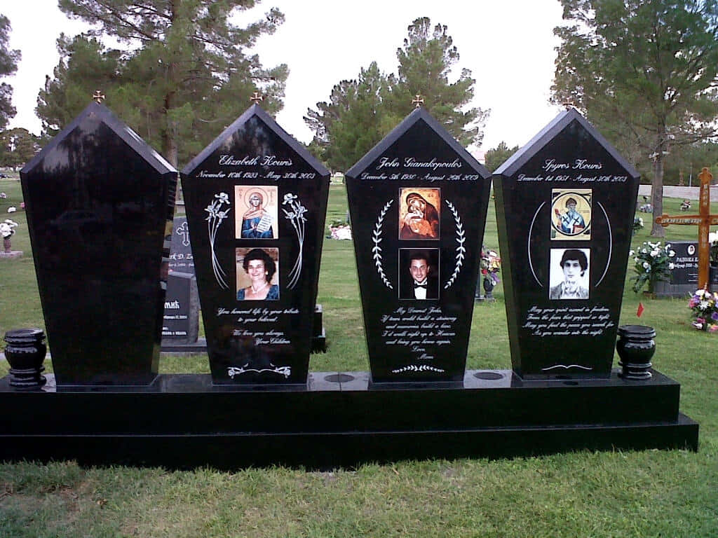 Memorial 桌布 壁紙 — 墓地裡的四塊黑色棺材形墓碑，每塊都展示著刻有照片和姓名的逝者，周圍環繞著綠草和樹木。