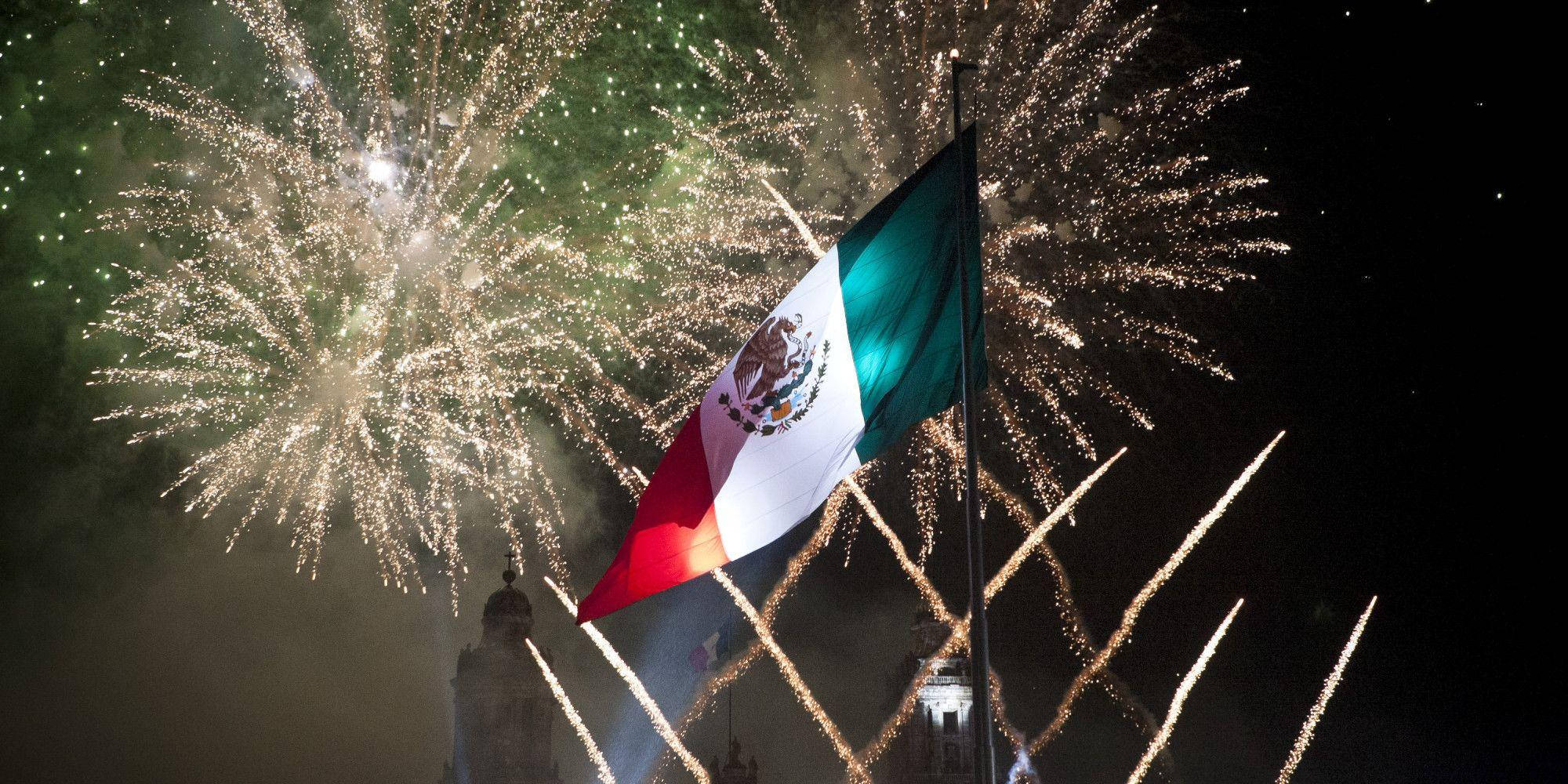 Independence 桌布 壁紙 — 墨西哥國旗在黑暗的天空中自豪地飄揚，壯觀的煙火綻放出鮮豔的綠色和金色光芒。