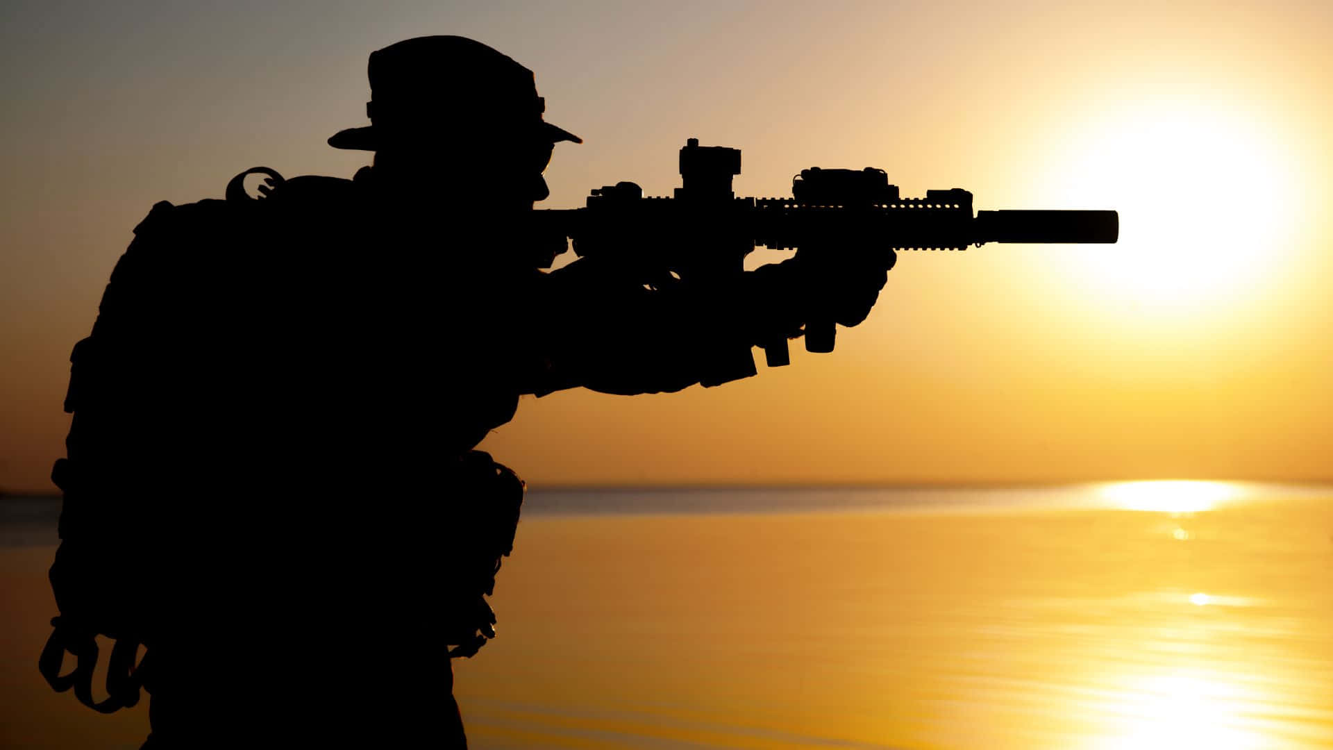 軍事動圖 桌布 壁紙 — 士兵剪影在日落時分於平靜水面上瞄準步槍，帶有金色光芒。