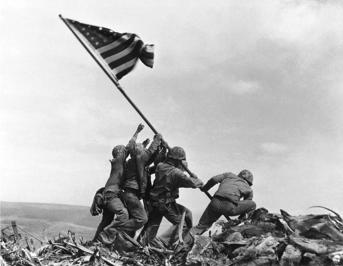 Ww2 桌布 壁紙 — 士兵在戰場山脊上，在瓦礫和陰天中升起美國國旗。