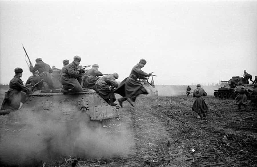 soldier 桌布 壁紙 — 士兵在泥濘的田野中從坦克跳下，煙霧在戰時陰沉天空下翻騰。