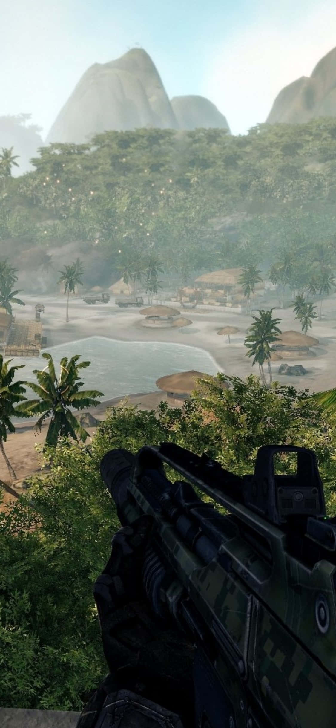 iPhone Xs Crysis Warhead 桌布 壁紙 — 士兵手持步槍俯瞰熱帶海灘村莊，背景有棕櫚樹和霧氣繚繞的山脈的第一人稱視角。