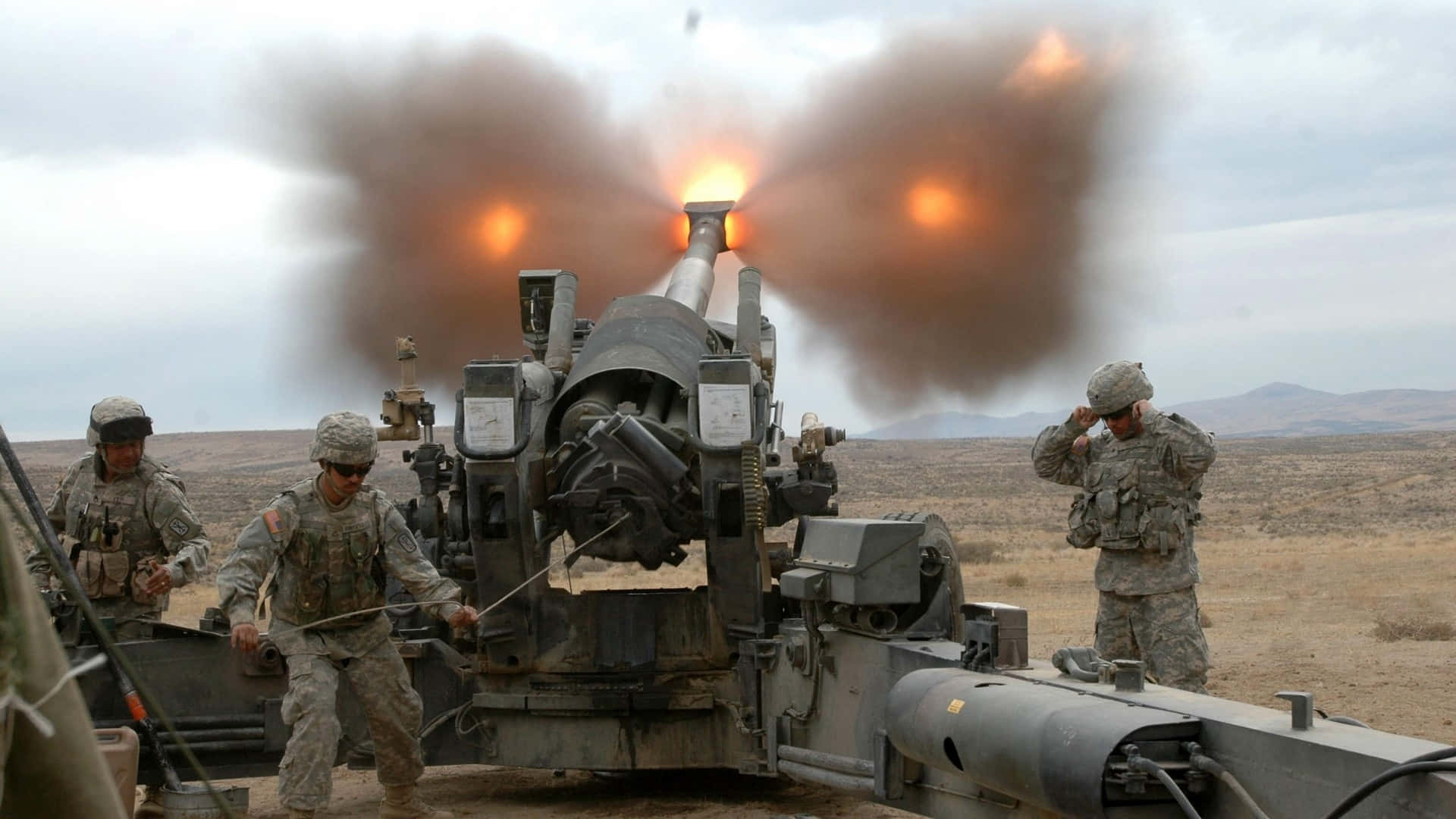 Marines 桌布 壁紙 — 士兵操作大型火炮在荒蕪的沙漠景觀中射擊，炮管冒出濃煙和火焰。