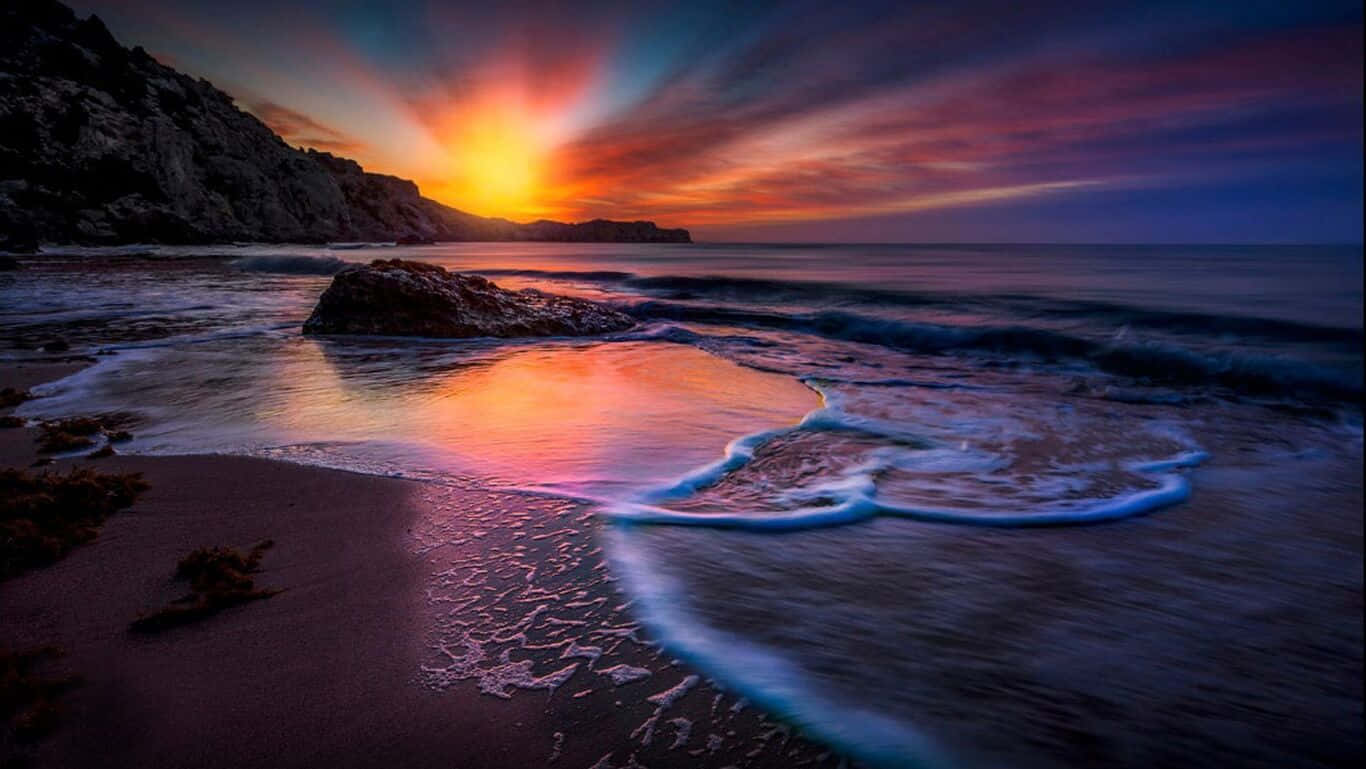 HD Beach 桌布 壁紙 — 壯麗的夕陽將海洋和懸崖染成火熱的橙色和深紫色，海浪輕輕拍打海岸。