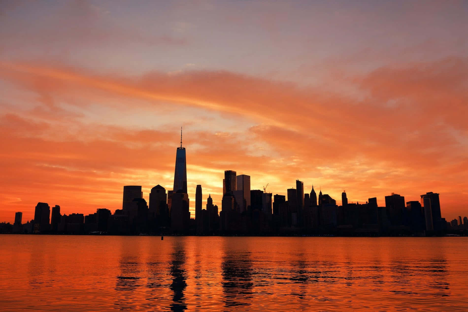 New York 桌布 壁紙 — 壯麗的日落將紐約市天際線染成火熱的橙色，其輪廓倒映在平靜的水面上。