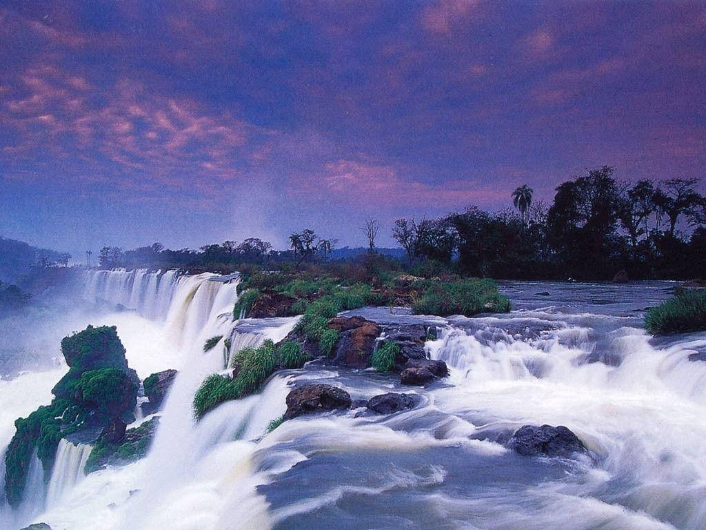 Zambia 桌布 壁紙 — 壯麗的瀑布在戲劇性的紫色和粉紅色暮色天空下，從長滿苔蘚的岩石上傾瀉而下。