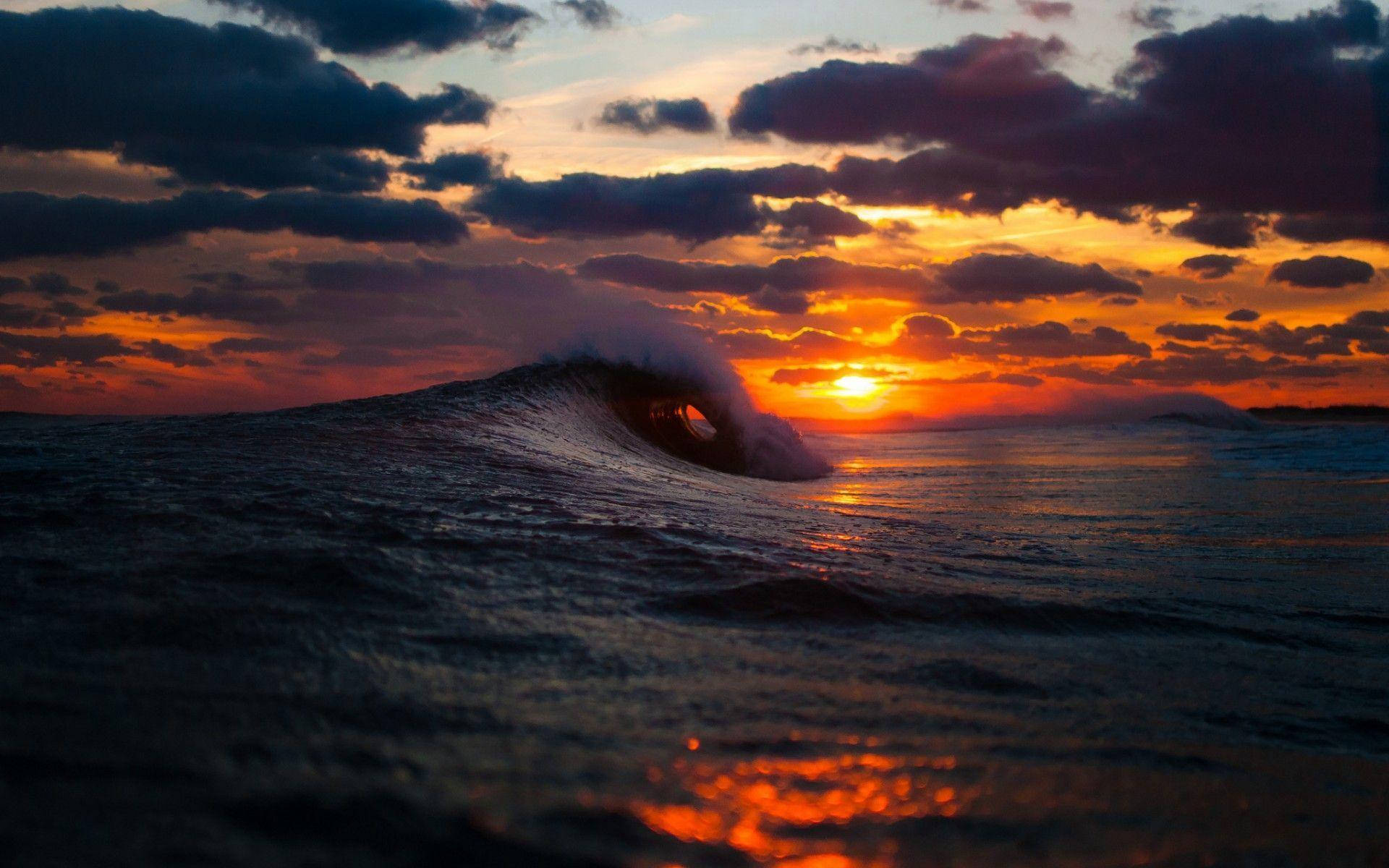日落 桌布 壁紙 — 夕陽下，一道戲劇性的海浪捲成完美的管狀，上方有火橙和紫色的雲彩。