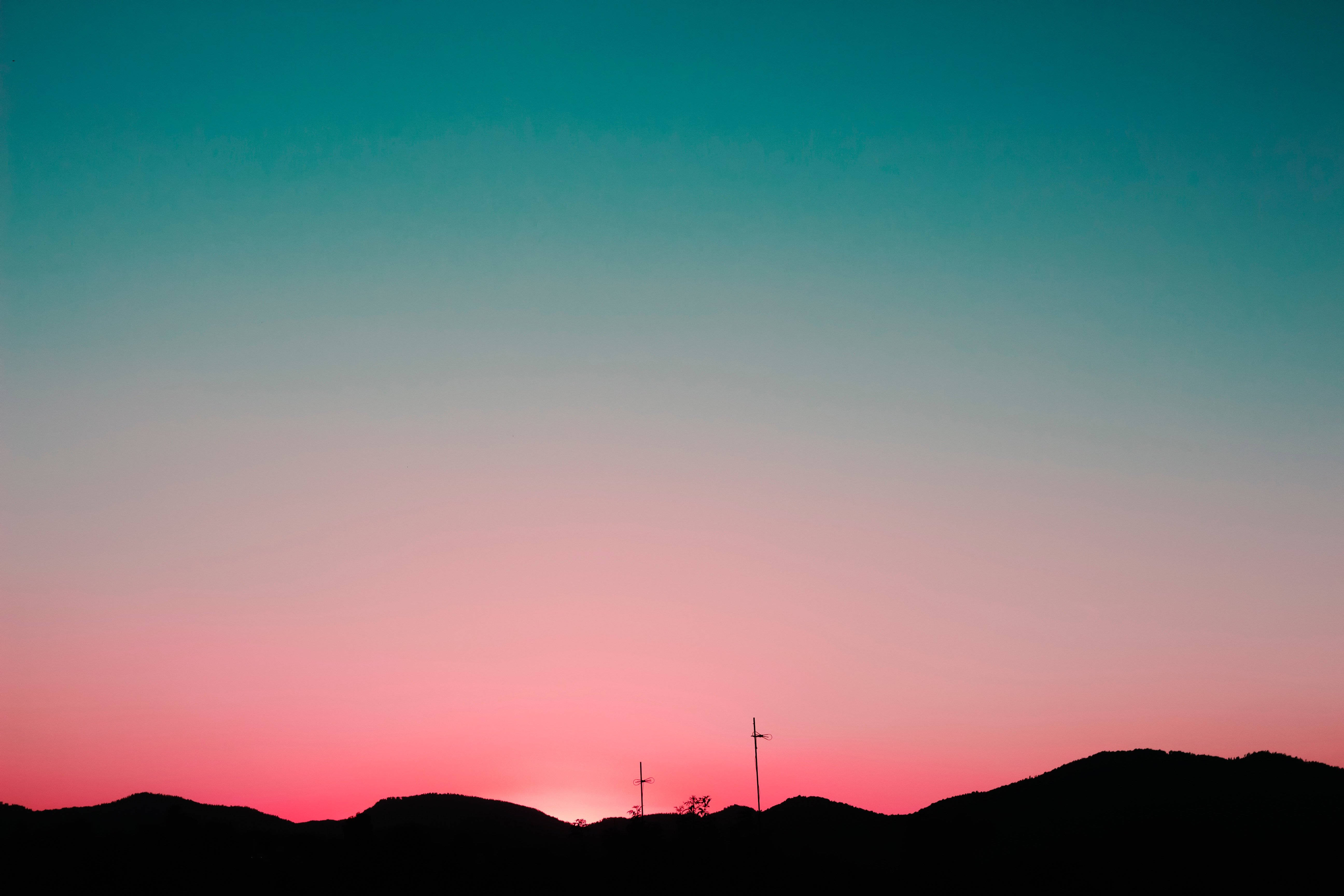 山脈 桌布 壁紙 — 夕陽下，剪影山丘和無線電塔映襯著青綠色和粉紅色的漸變天空。