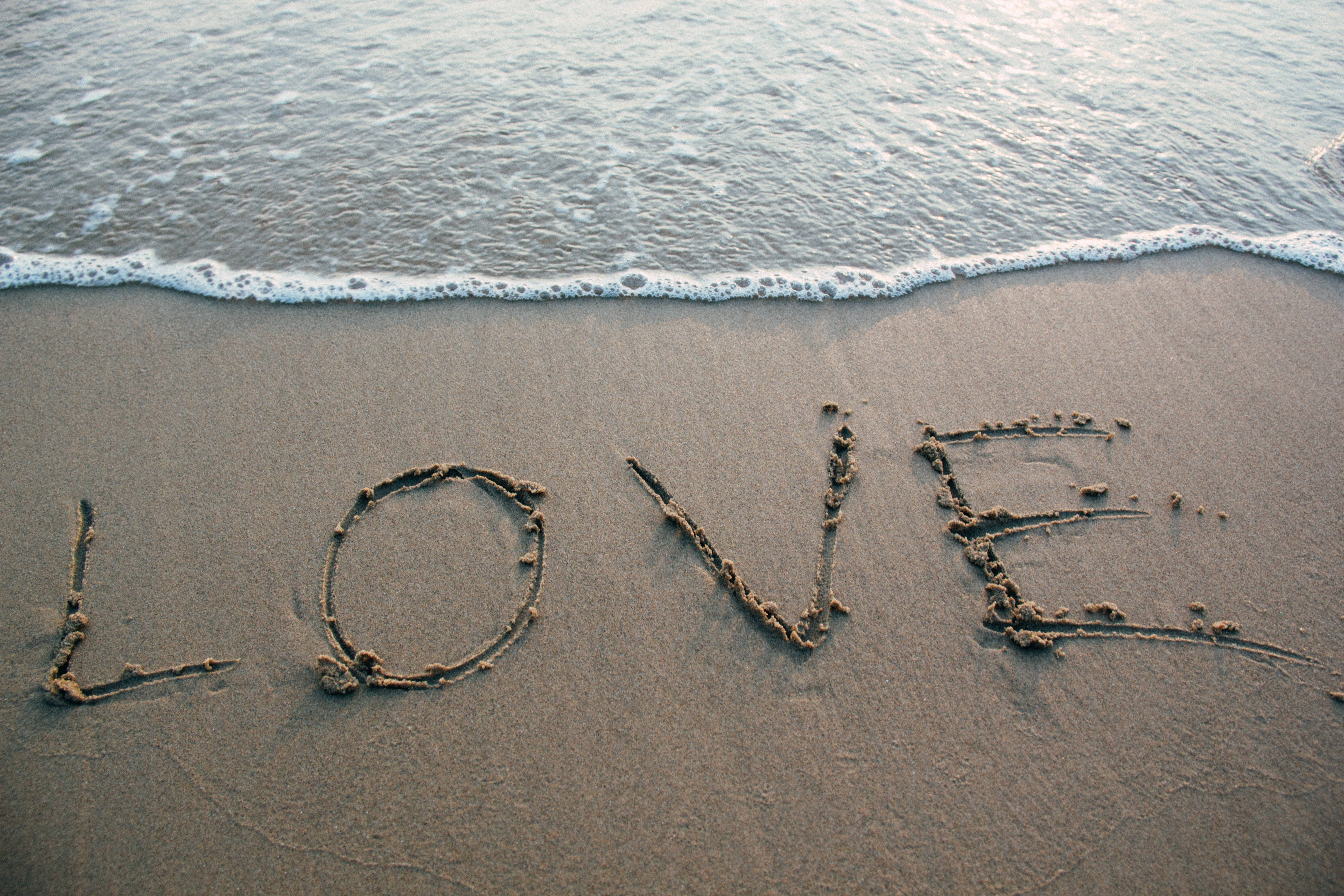 Romantic Love 桌布 壁紙 — 夕陽下，溫柔的海浪拍打著濕沙，沙上寫著「LOVE」這個詞。