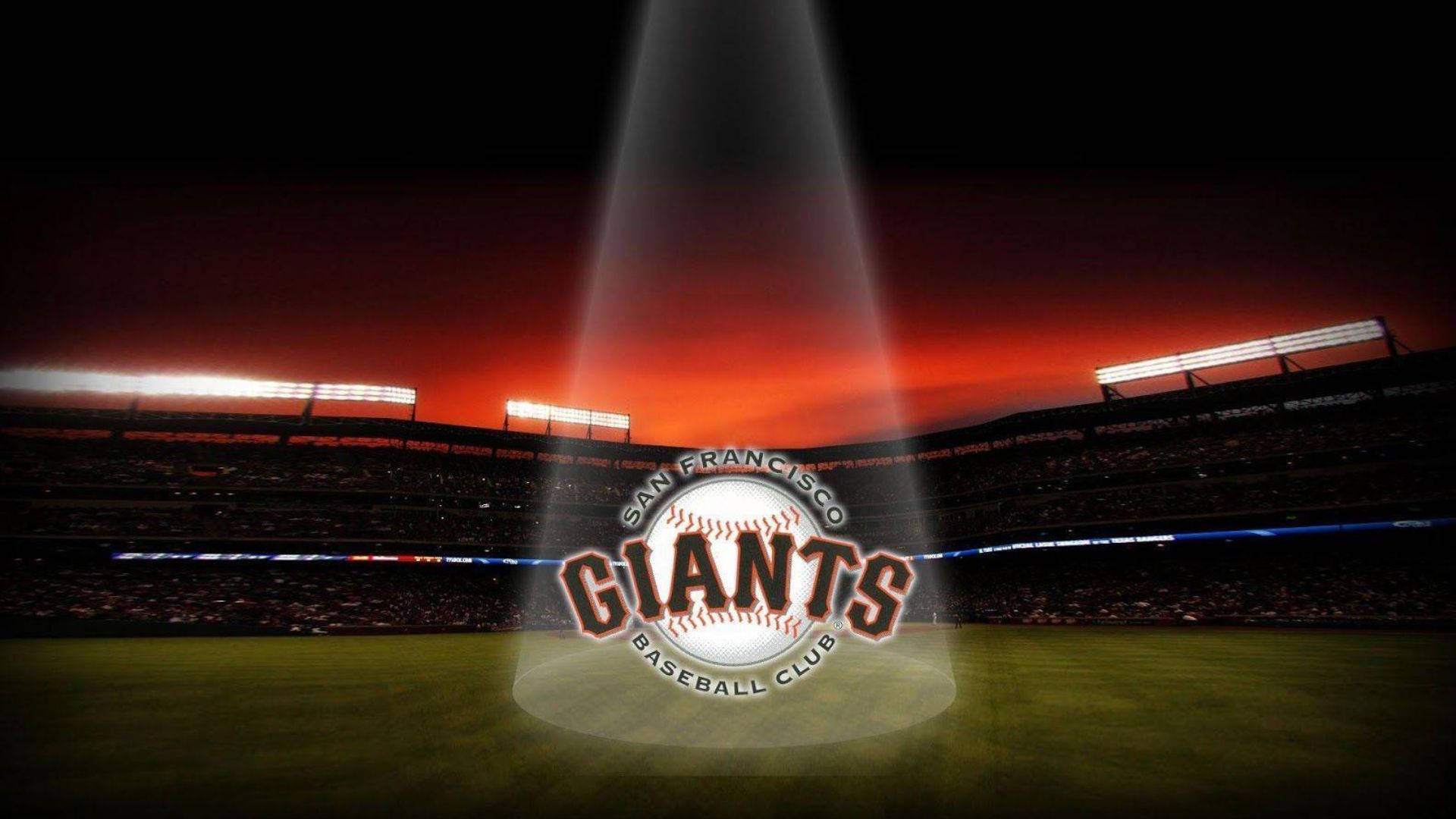 Giants 桌布 壁紙 — 夕陽下，聚光燈照射在球場中央的舊金山巨人隊棒球標誌上。