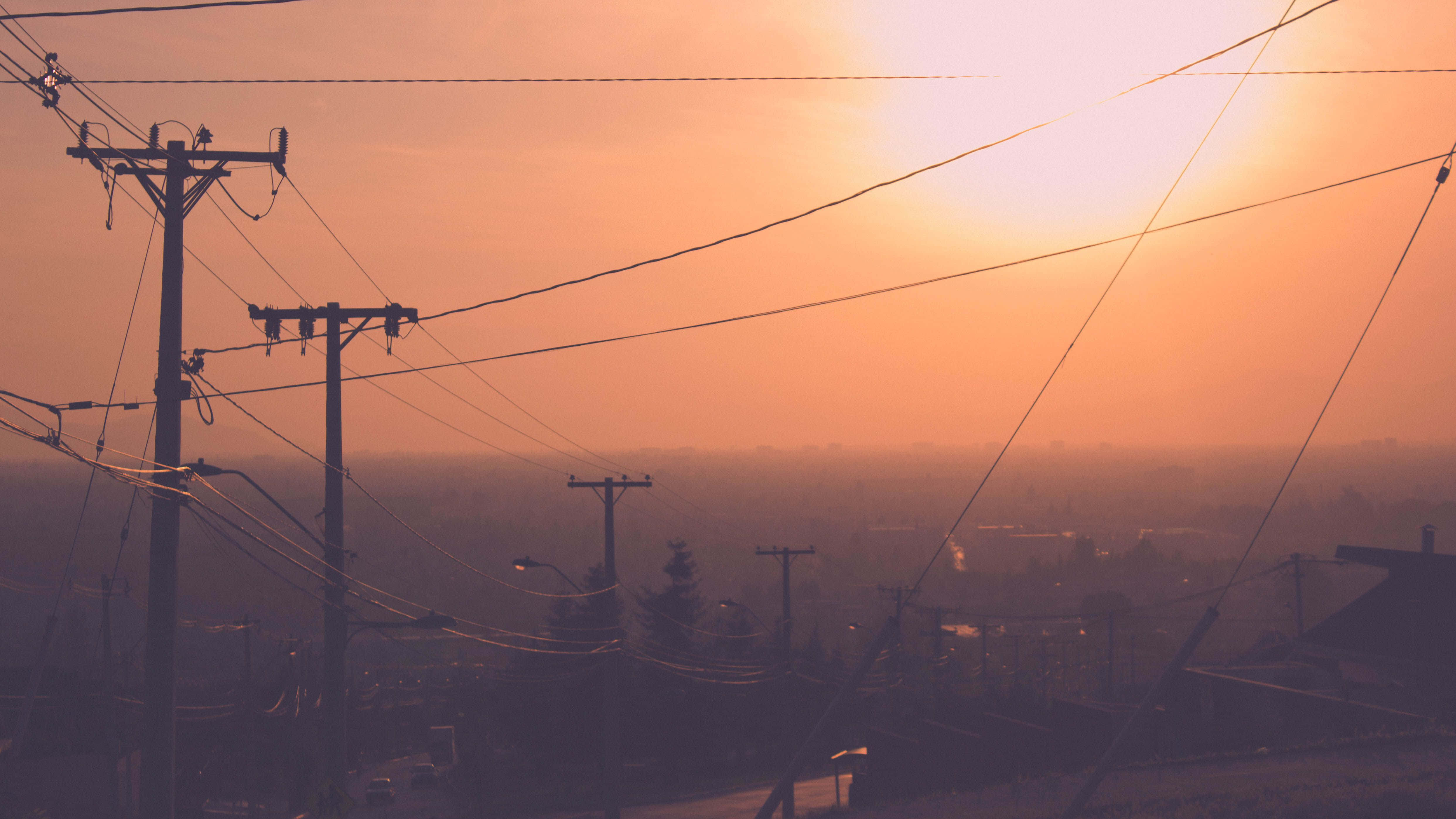 Chill Aesthetic 桌布 壁紙 — 夕陽下，遠方城市景觀上空朦朧的橙色天空中，輪廓分明的電線縱橫交錯。