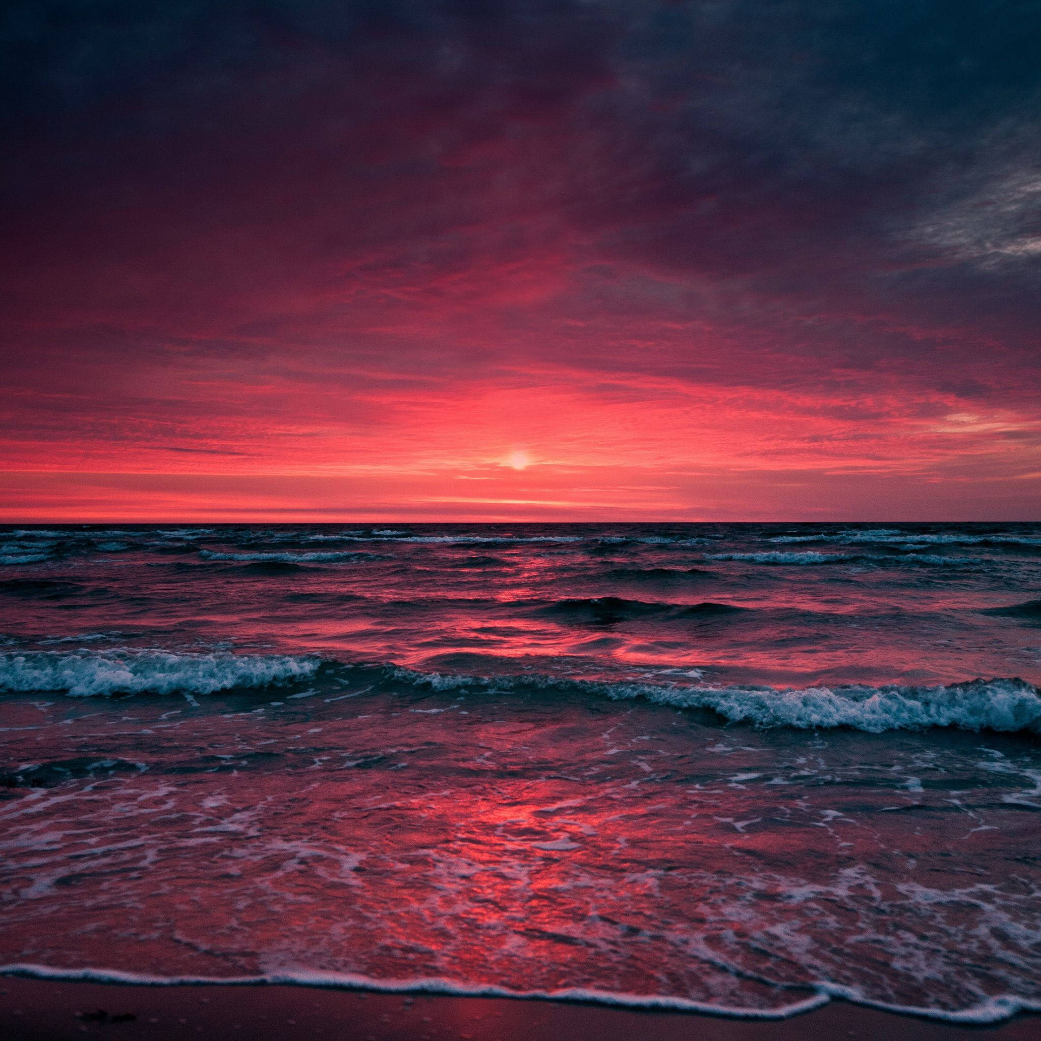iPad 桌布 壁紙 — 夕陽下壯麗的海洋，火紅和深紫色的雲彩生動地映照在翻騰的海浪上。
