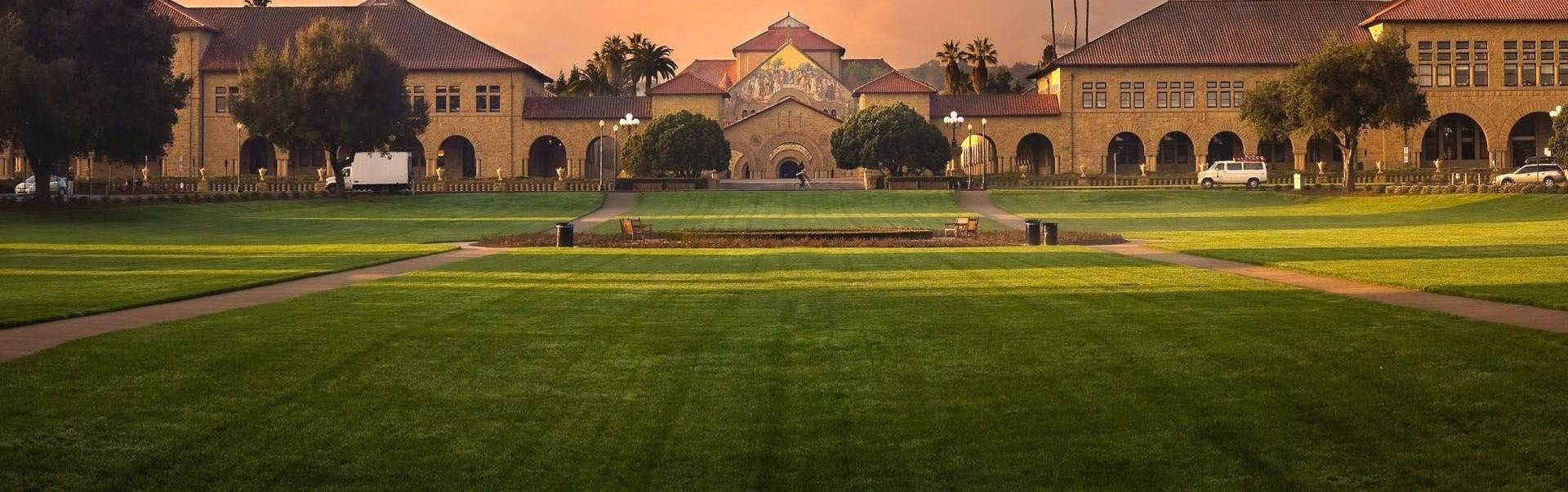 field 桌布 壁紙 — 夕陽下宏偉的大學校園，金色光芒照亮歷史建築和修剪整齊的草坪。