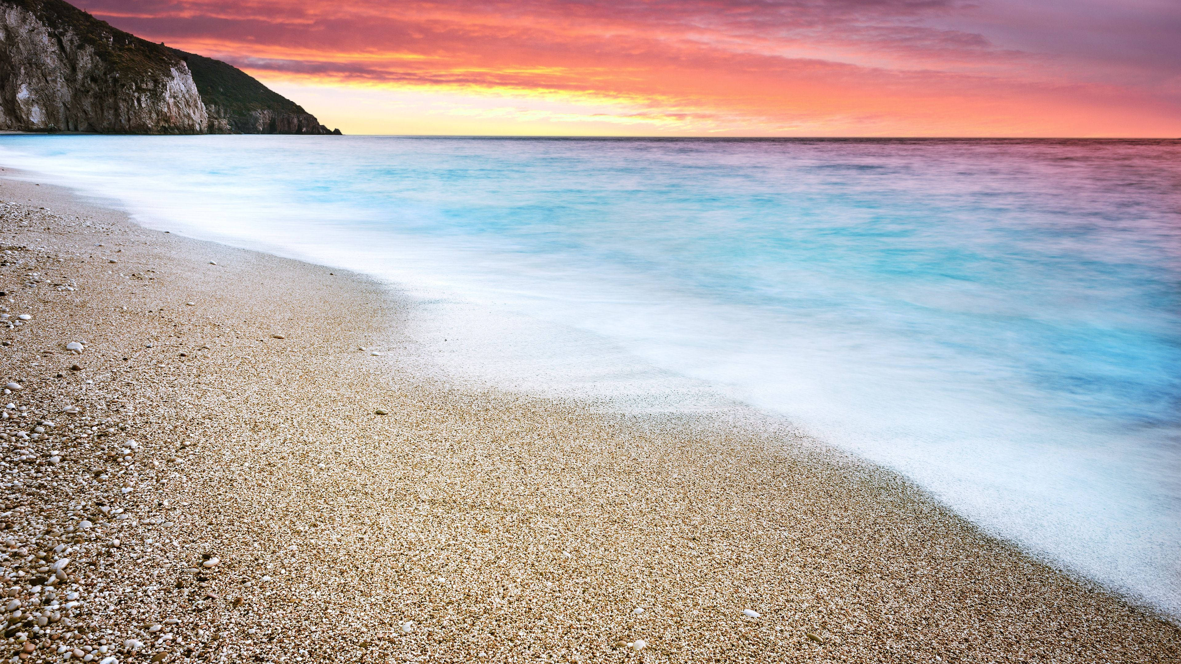 Beach Sunset HD 桌布 壁紙 — 夕陽下寧靜的海灘，在火紅橙和粉紅色的天空下，碧綠色的海浪輕輕拍打著卵石灘。