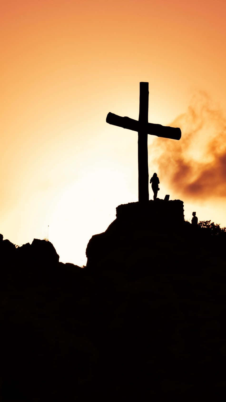 Jesus iPhone 桌布 壁紙 — 夕陽下岩石山峰上的十字架剪影，兩個人影虔誠地站立在火紅橙色的天空前。