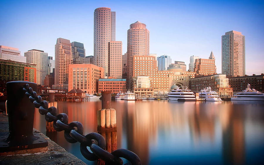 Massachusetts 桌布 壁紙 — 夕陽以溫暖的光線沐浴著港口城市景觀，摩天大樓在停泊遊艇旁的平靜水面上倒映。