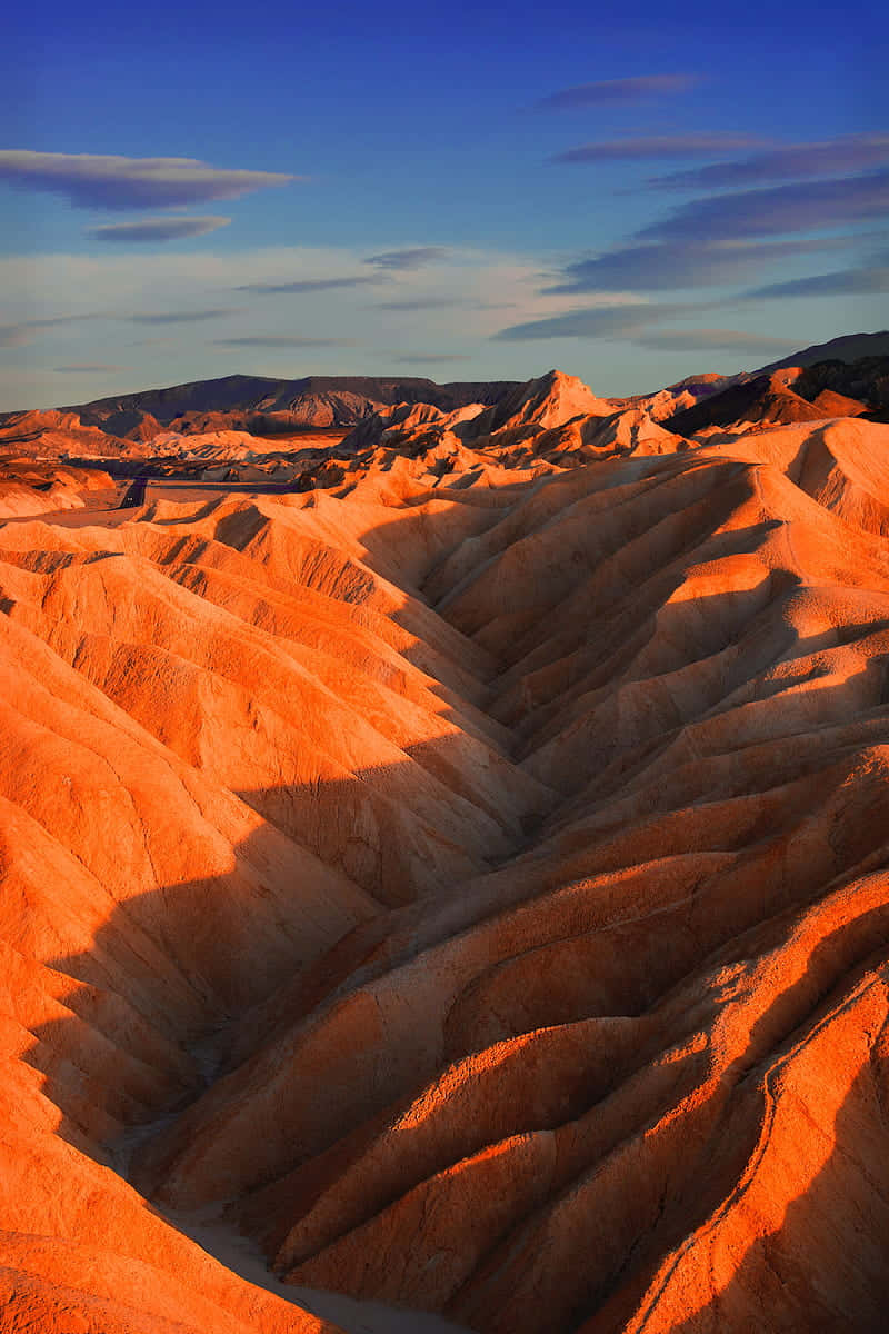 Geomorphology 桌布 壁紙 — 夕陽以溫暖的光線沐浴著起伏的橙色岩層，背景是深藍色的天空和散落的雲朵。
