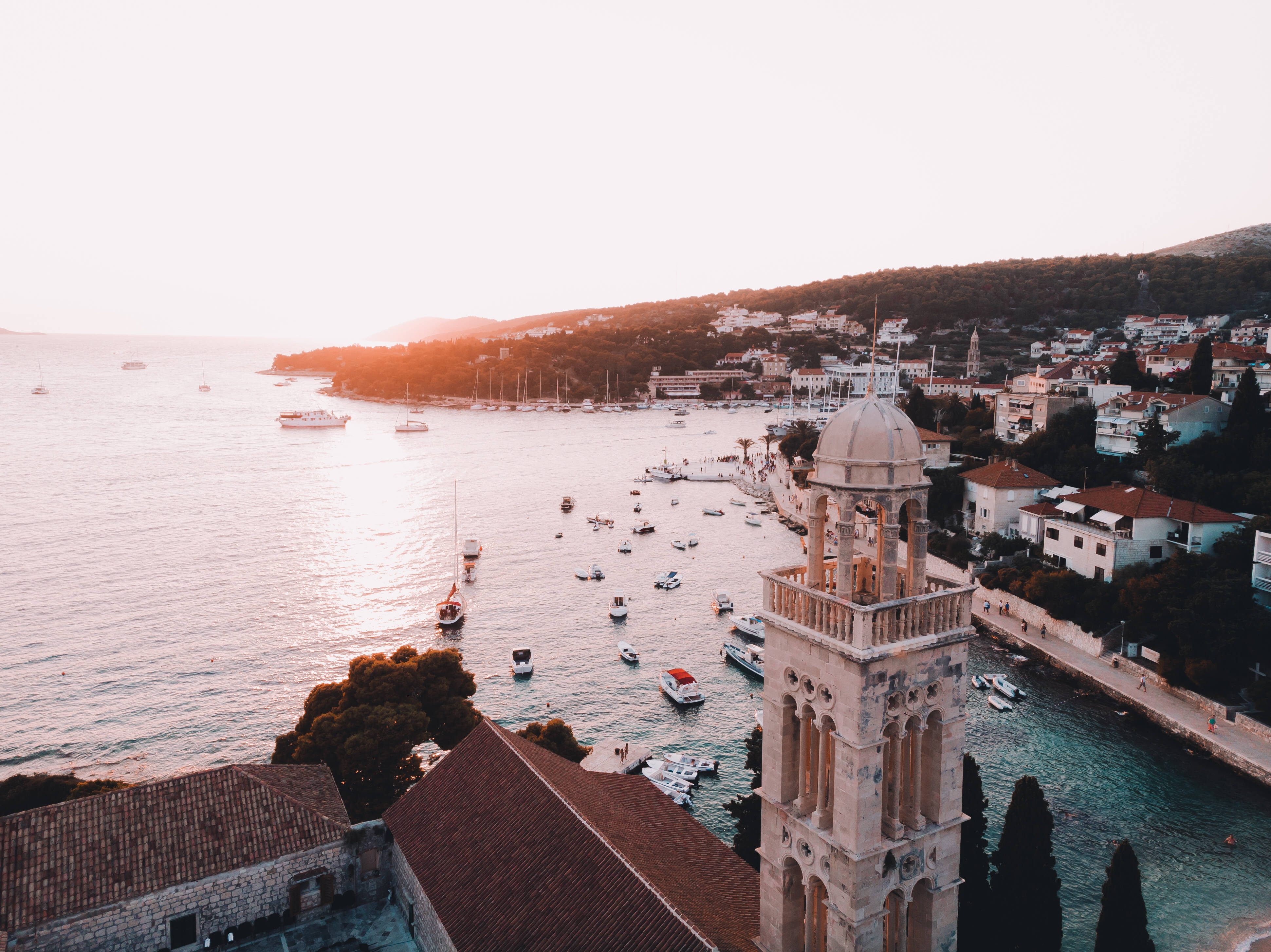 Croatia 桌布 壁紙 — 夕陽以溫暖的光芒沐浴著沿海小鎮，船隻點綴在平靜的海面上，旁邊是歷史悠久的石建築和一座突出的鐘樓。