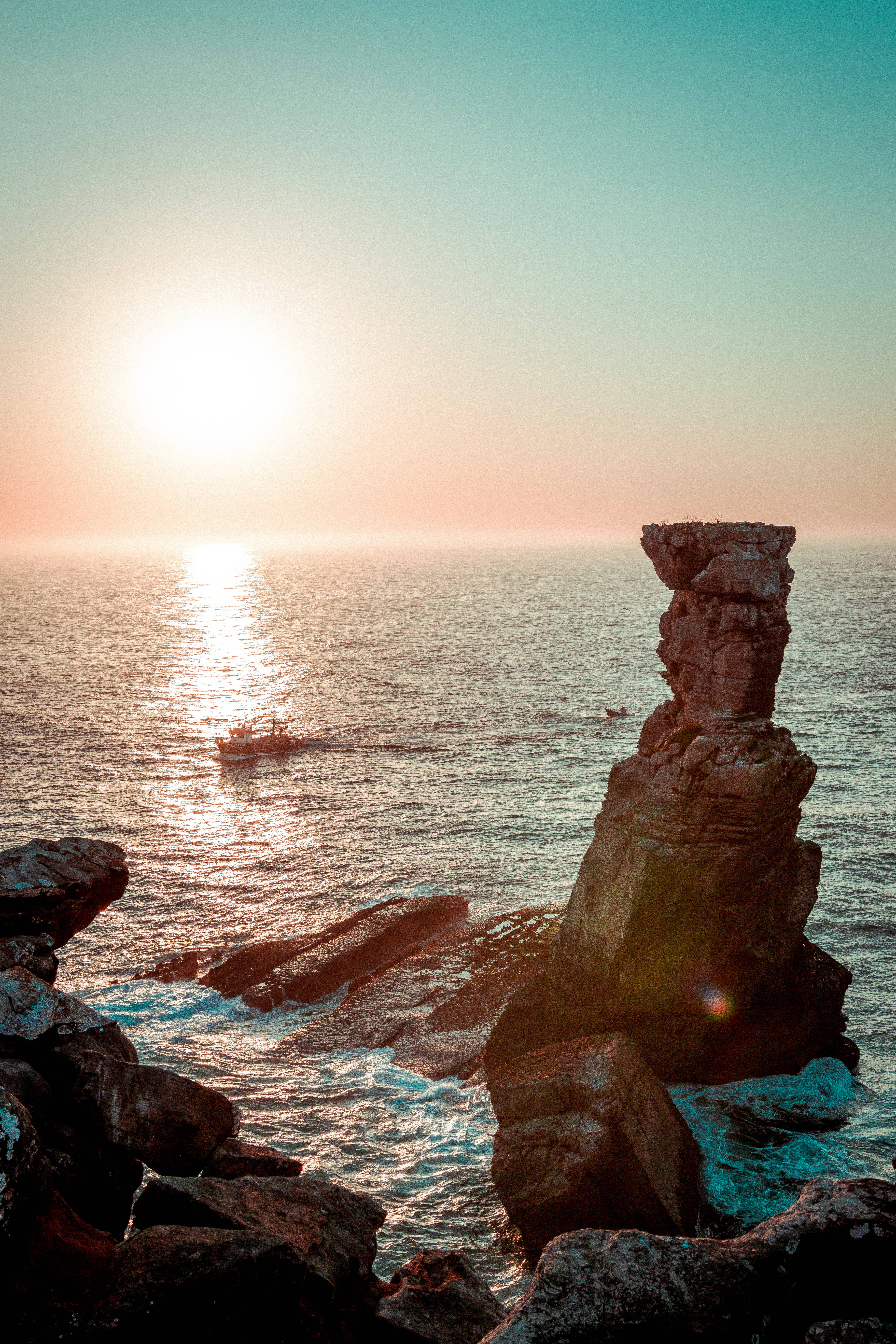 Cabo 桌布 壁紙 — 夕陽以溫暖的光芒沐浴著高聳的海蝕柱，一艘小船在平靜的海平線上滑行。
