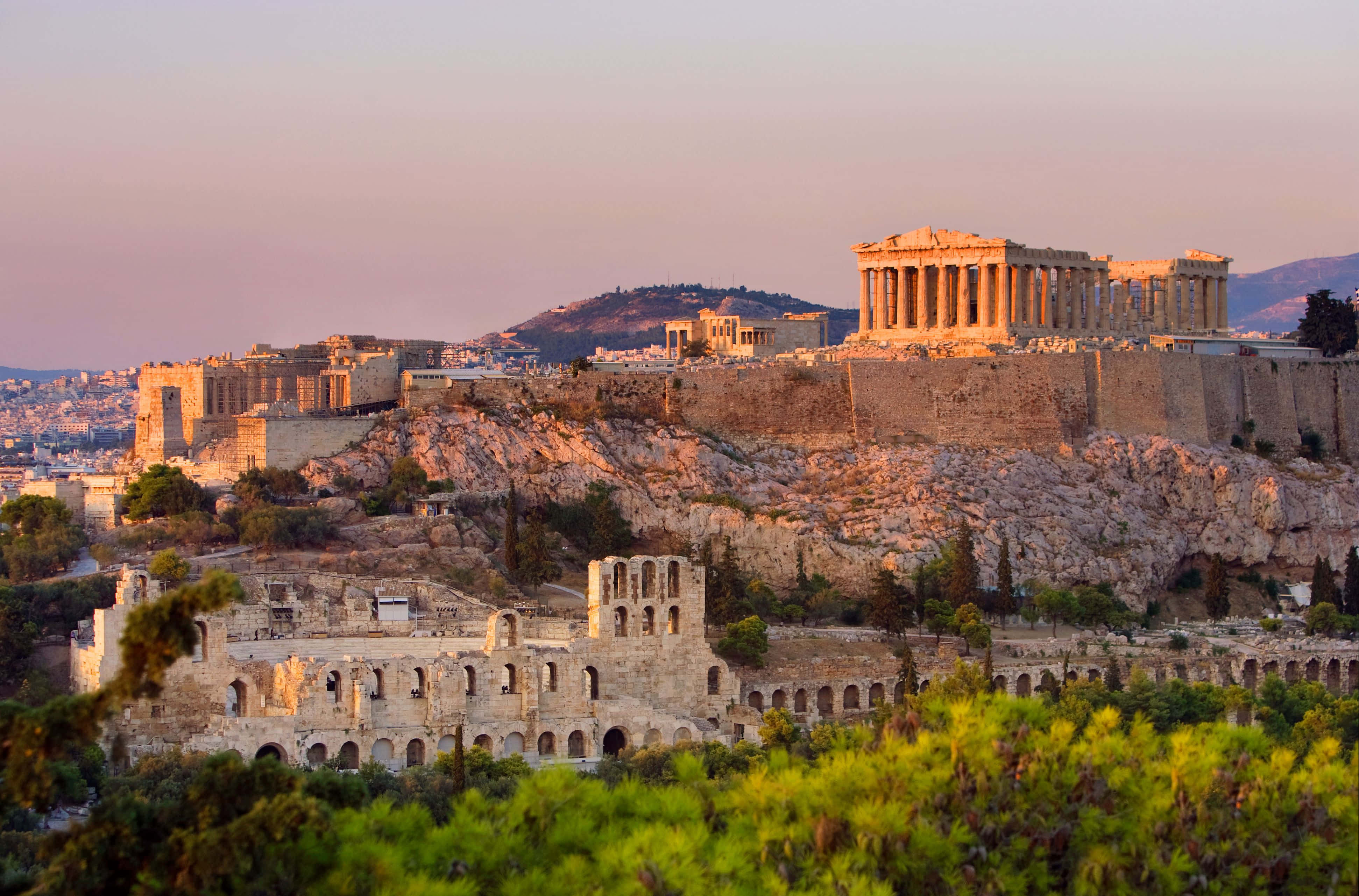 greek 桌布 壁紙 — 夕陽以溫暖的金色光芒沐浴著古老的帕德嫩神廟和衛城，映襯著柔和的粉紅色天空。