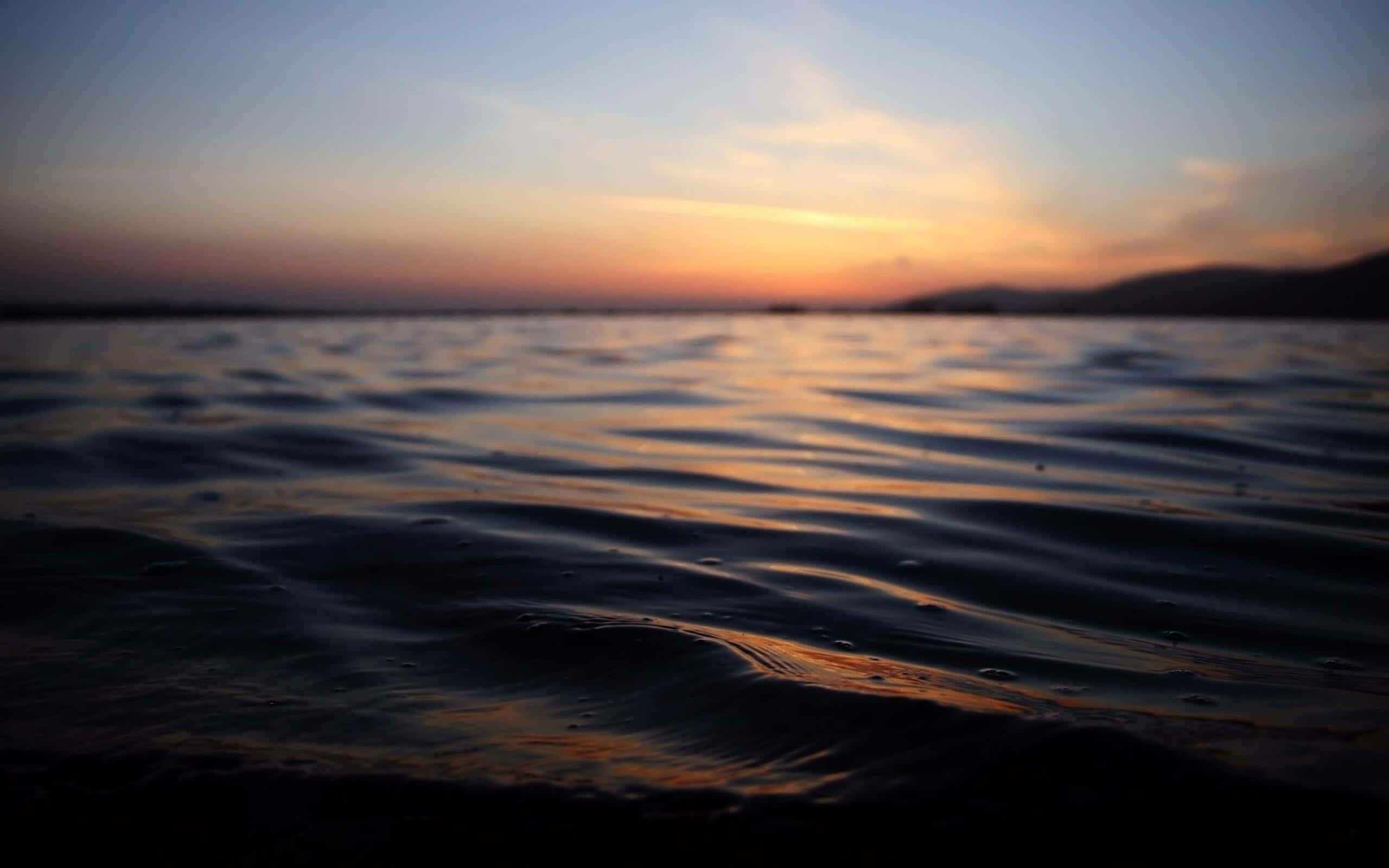 放鬆 桌布 壁紙 — 夕陽以溫暖色調塗抹天空，倒映在漣漪的水面上，遠山在漸暗的光線中呈現剪影。
