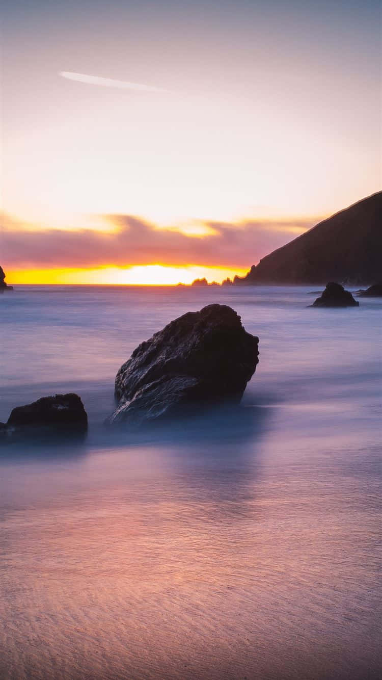 Beautiful Beach 桌布 壁紙 — 夕陽以溫暖色調塗抹天空，平滑的水流繞過海岸懸崖附近的深色岩石。