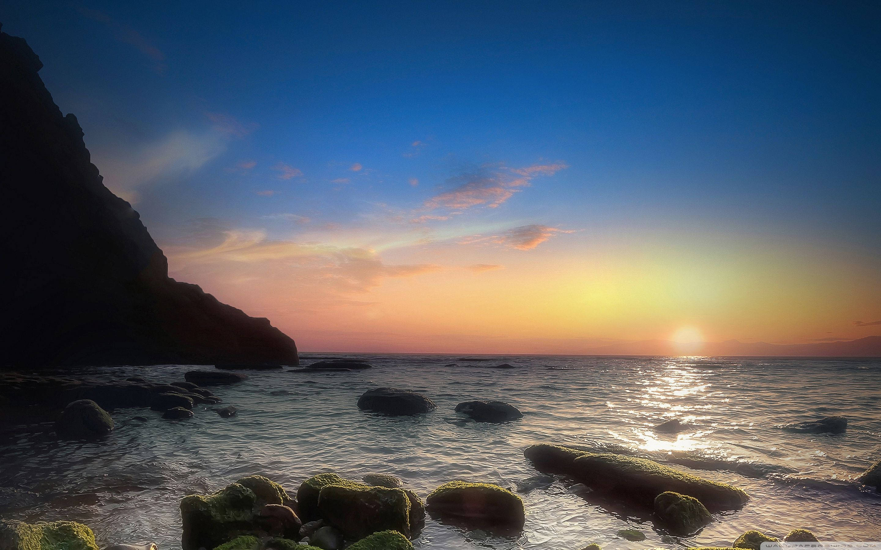 Naples 桌布 壁紙 — 夕陽以溫暖色調塗抹天空，海浪輕輕拍打著黑暗懸崖旁長滿苔蘚的岩石。