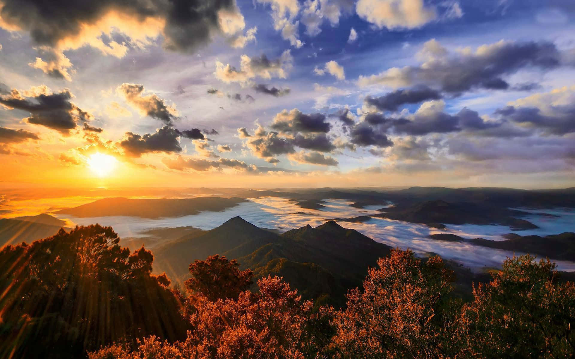 太陽 桌布 壁紙 — 夕陽以金色光芒沐浴山頂和山谷雲層，呈現鮮豔的橙色和紫色色調。