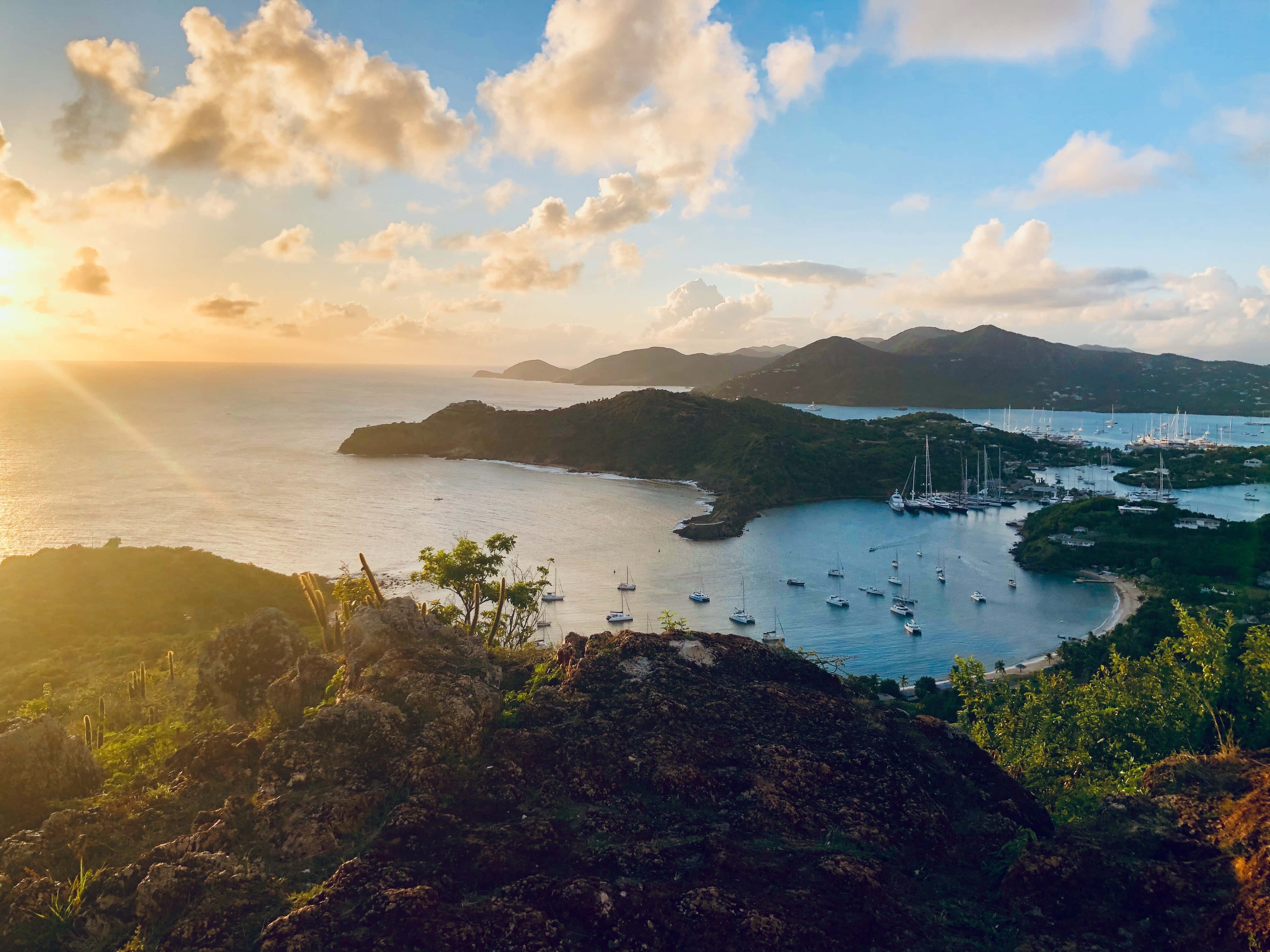 加勒比海 桌布 壁紙 — 夕陽以金色光芒沐浴熱帶海灣，帆船點綴在翠綠山丘環抱的平靜碧綠海水之間。