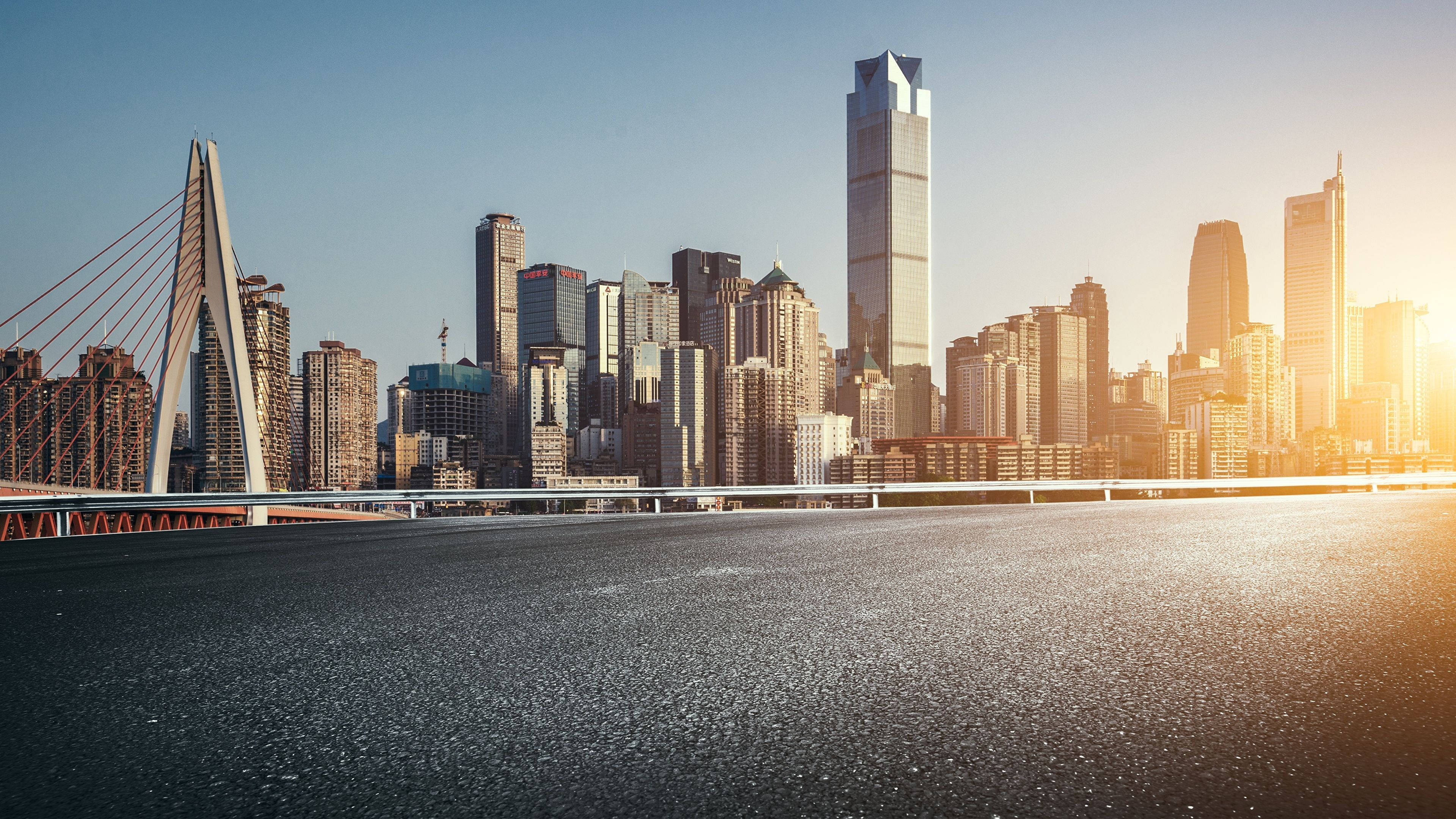 Chongqing 桌布 壁紙 — 夕陽以金色光芒沐浴現代城市景觀，一座橋樑橫跨寬闊的河流，摩天大樓在後方聳立。