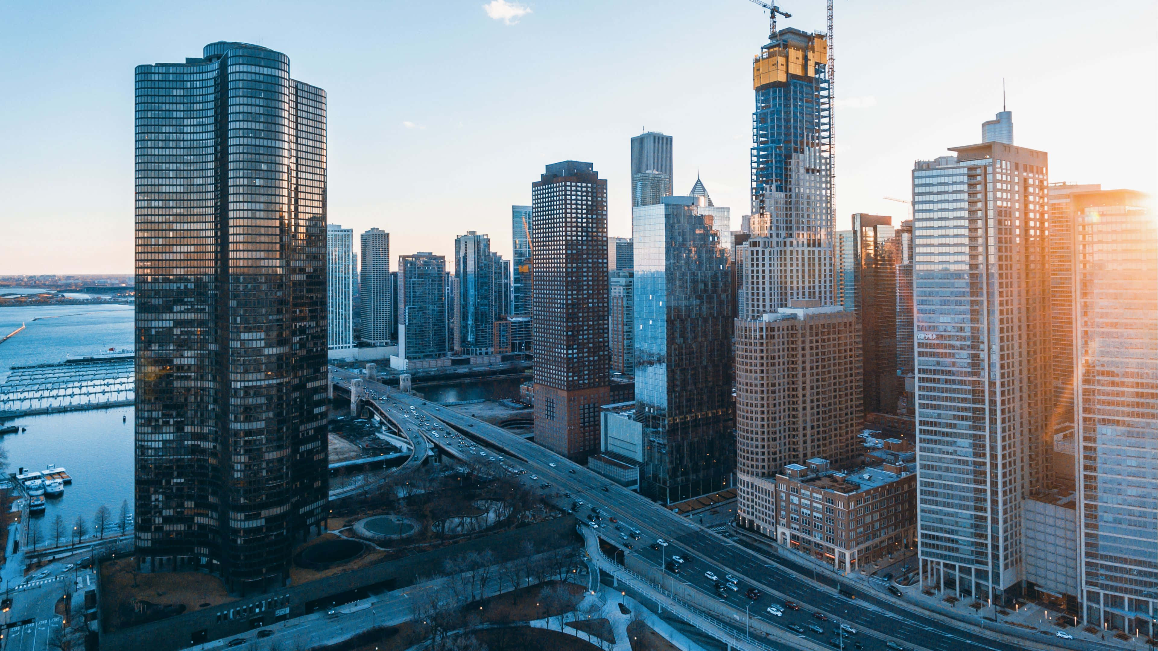 4K Ultra HD Chicago 桌布 壁紙 — 夕陽以金色光芒沐浴現代城市景觀，摩天大樓映照天空，河流蜿蜒穿過城市擴展區。