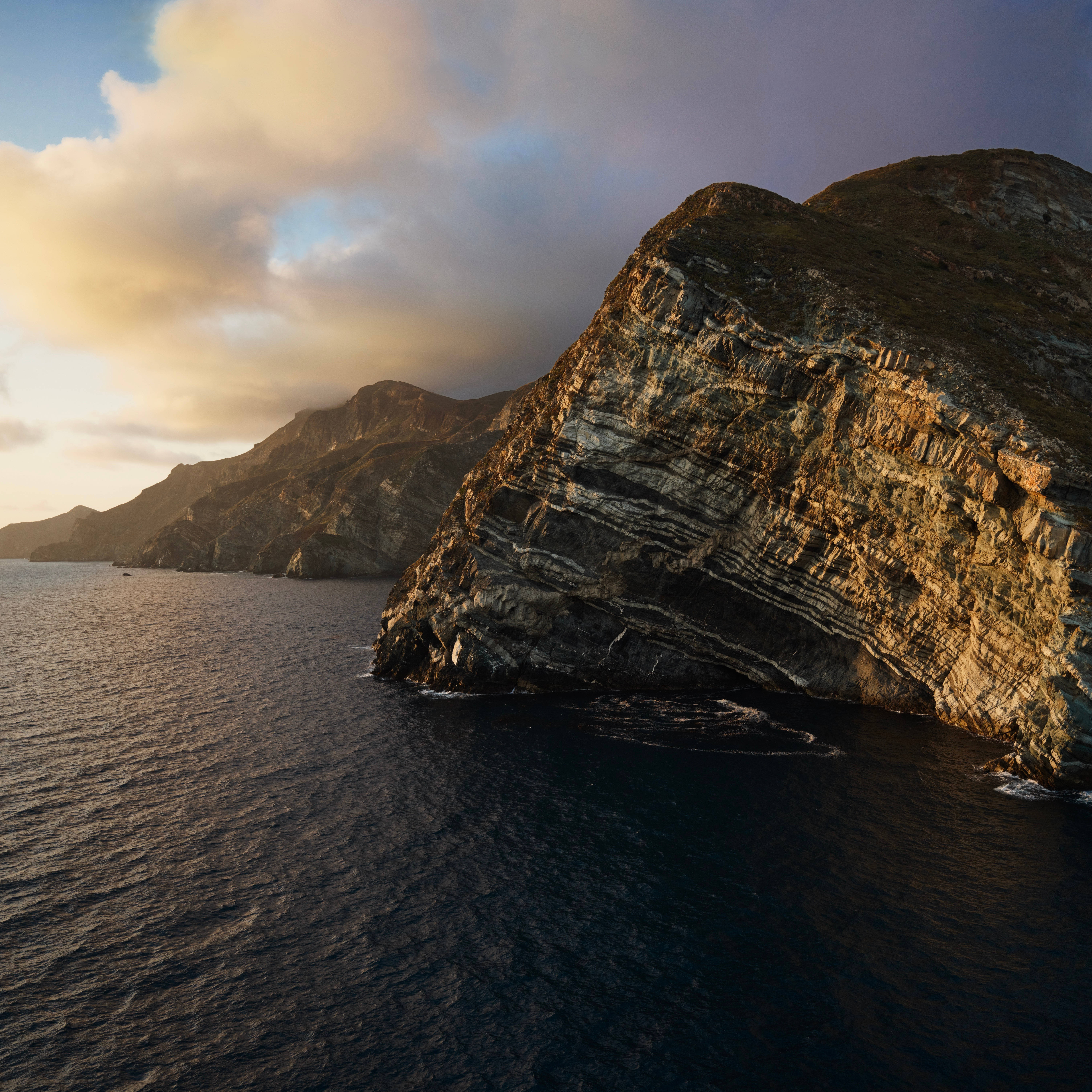 島嶼 桌布 壁紙 — 夕陽以金色光芒沐浴著戲劇性的層疊懸崖，海浪拍打其崎嶇的基部。