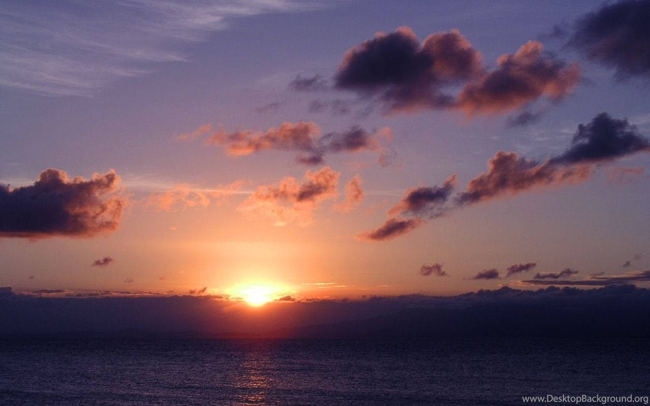 波多黎各 桌布 壁紙 — 夕陽以鮮豔的橙色和紫色渲染天空，雲朵在平靜的海洋上反射著太陽的光芒。