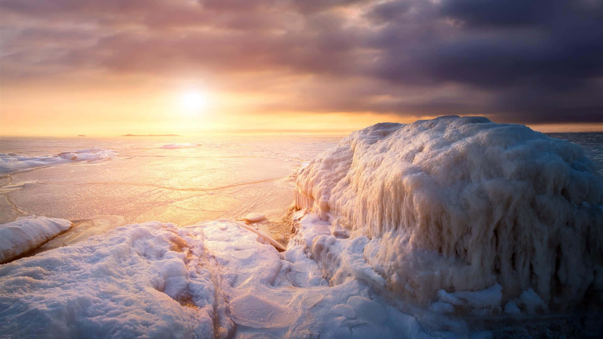 Winter Beach 桌布 壁紙 — 夕陽在冰冷的水面上閃耀，前景有冰凍的懸崖和紋理冰層。