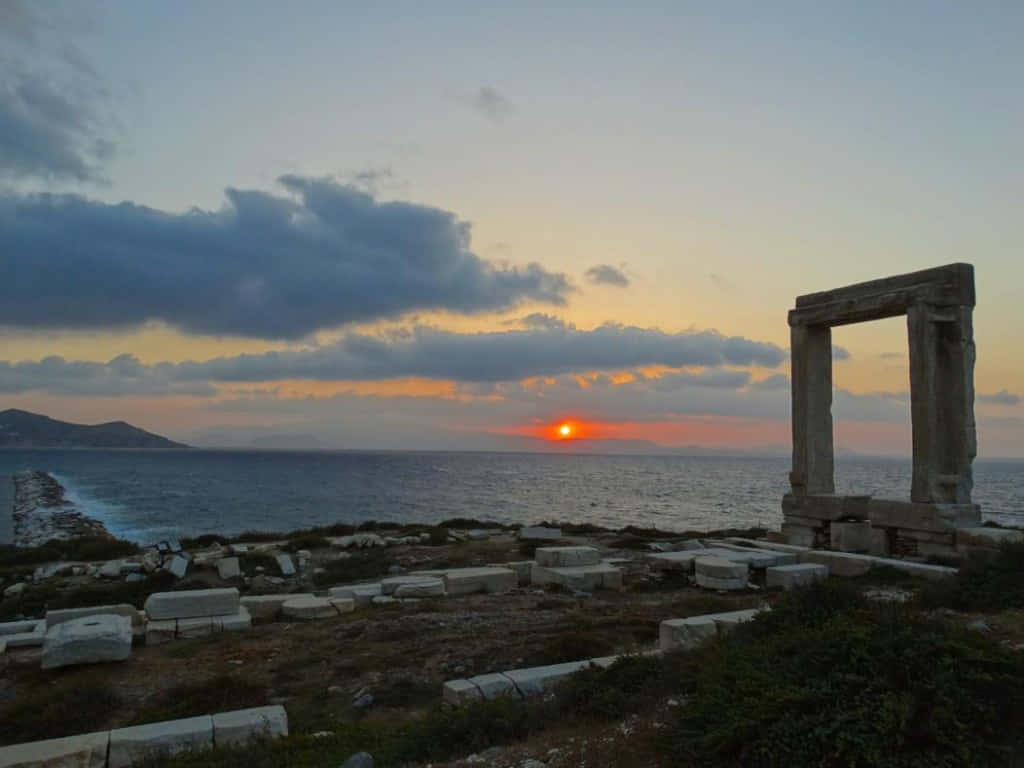 太陽 桌布 壁紙 — 夕陽在古老石頭廢墟後方發光，在黃昏時分以戲劇性的雲彩框住大海。