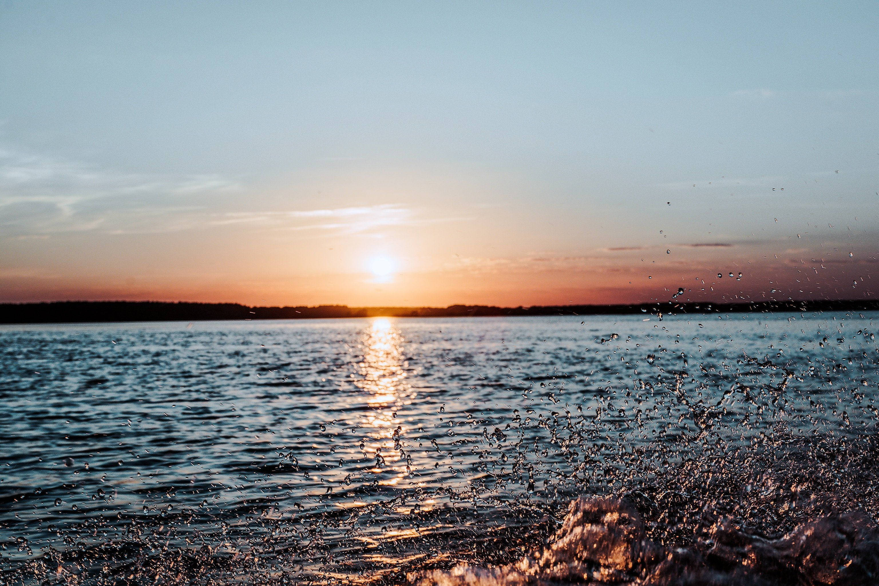 Sunset Aesthetic 桌布 壁紙 — 夕陽在平靜的水面上閃耀，前景的水花捕捉到金色的光芒。