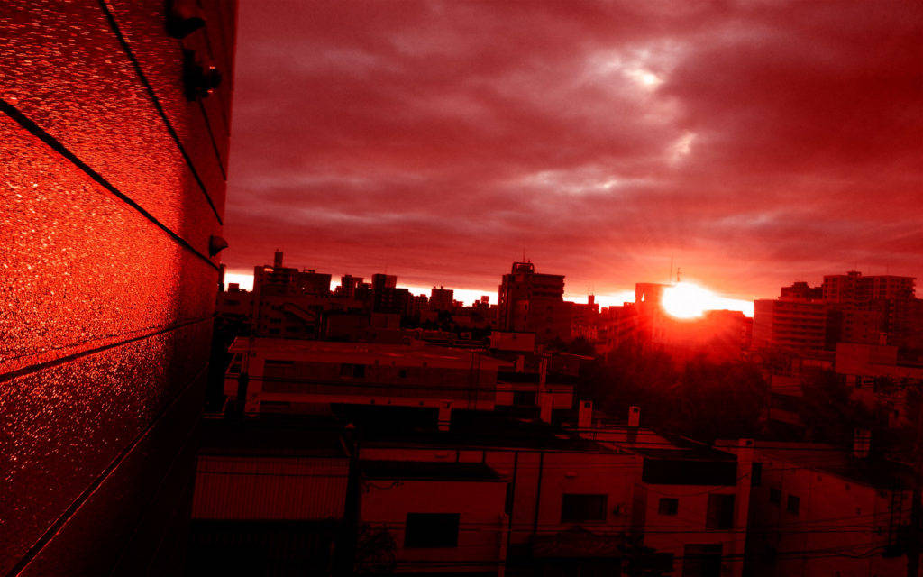 Red And Black Phone 桌布 壁紙 — 夕陽在建築物後方落下，城市景觀沐浴在強烈的紅光中，在紋理牆壁上投下長長的陰影和發光的倒影。