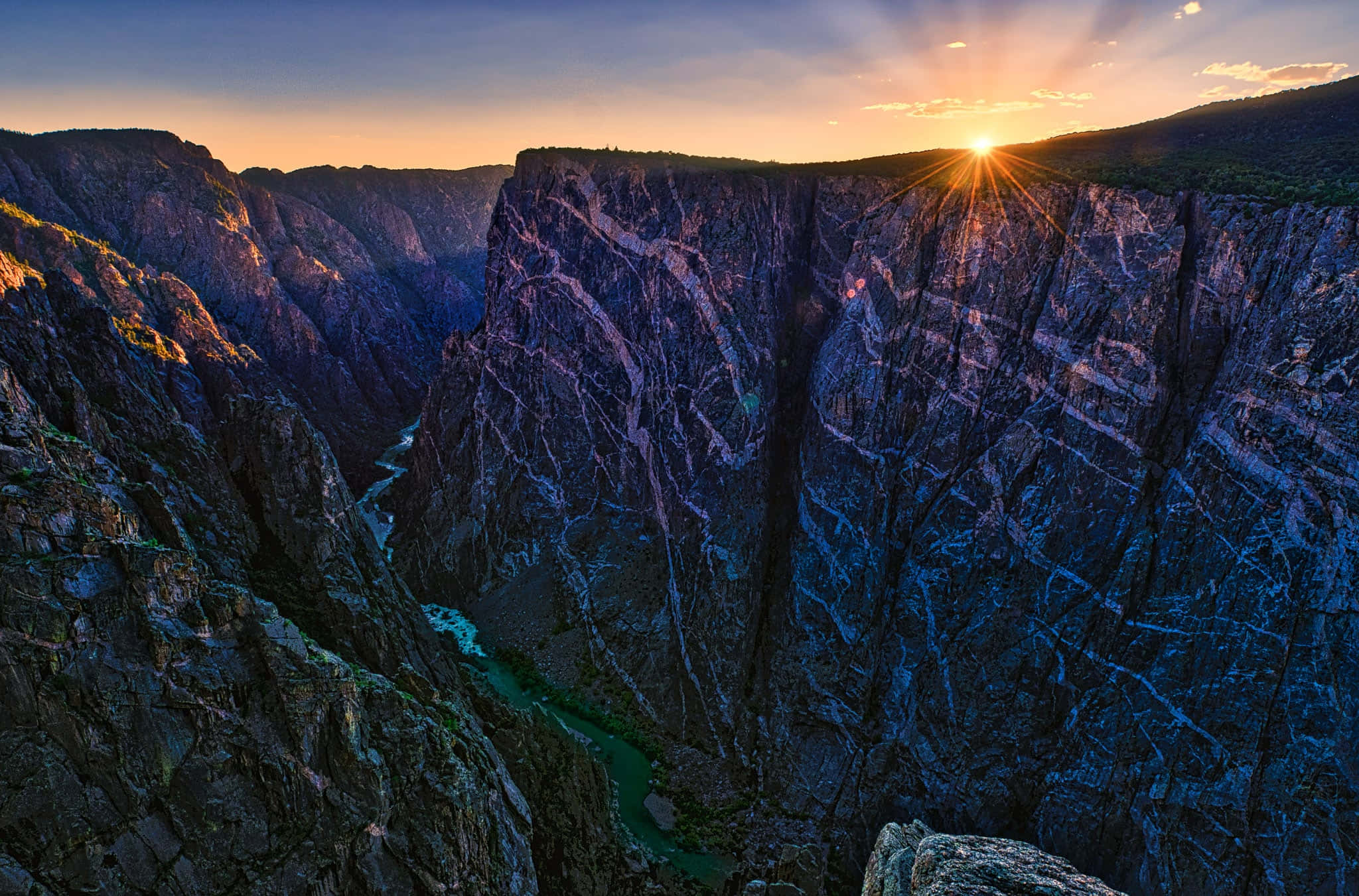 Black Canyon 桌布 壁紙 — 夕陽在深邃的峽谷上灑下金色光芒，一條碧綠色的河流蜿蜒穿過崎嶇的懸崖。