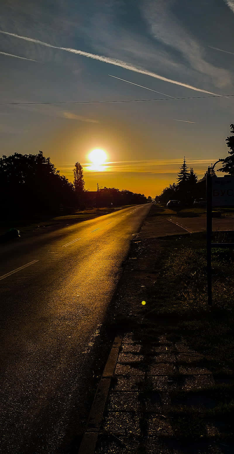 早安 桌布 壁紙 — 夕陽在濕漉漉的道路上投下金色光芒，樹木和飛機雲在暮色天空中。