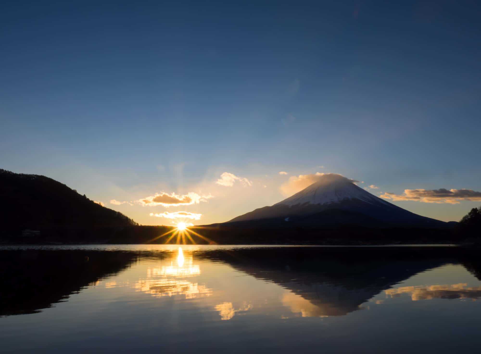 日出 桌布 壁紙 — 夕陽在積雪的富士山後方發光，完美倒映在平靜的湖水中，周圍是黑暗的森林山坡。