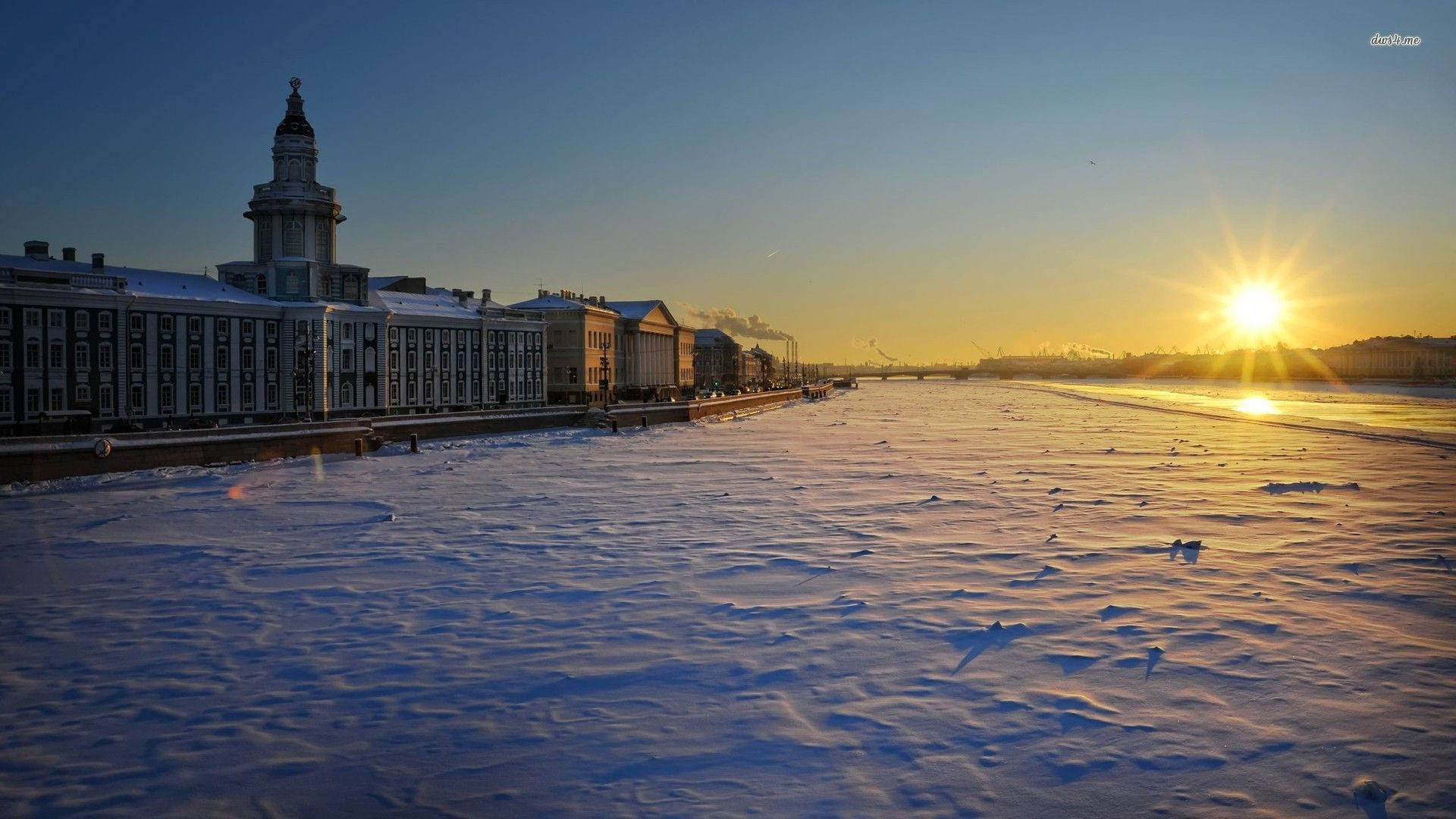 Saint Petersburg 桌布 壁紙 — 夕陽在結冰的河面上閃耀，河岸兩旁是積雪的歷史建築。
