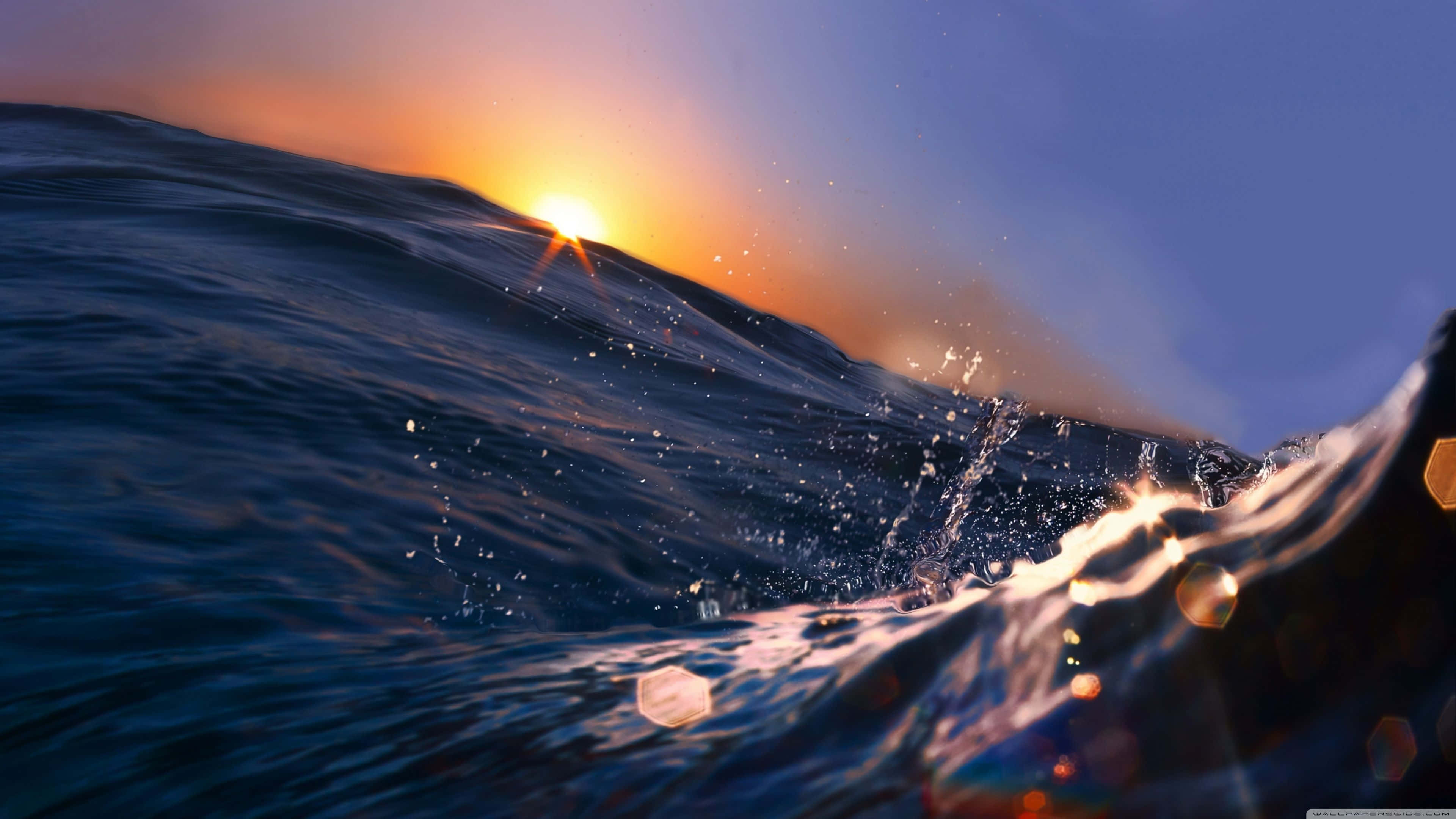 桌布 壁紙 — 夕陽在翻騰的海浪後發光，伴隨著閃爍的水滴和六邊形鏡頭光暈。