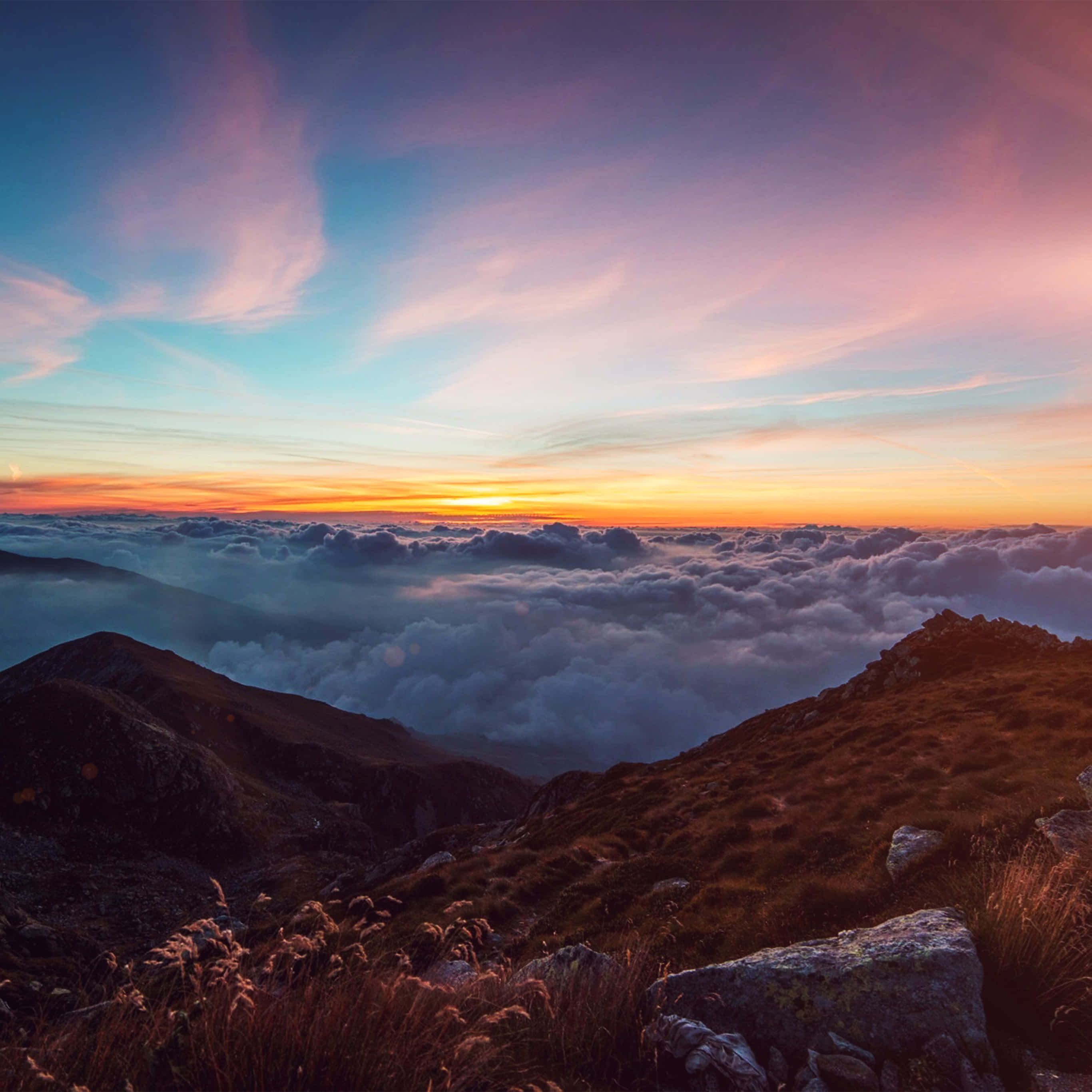 太陽 桌布 壁紙 — 夕陽在雲海之上繪出鮮豔的天空，前景是崎嶇的山峰。